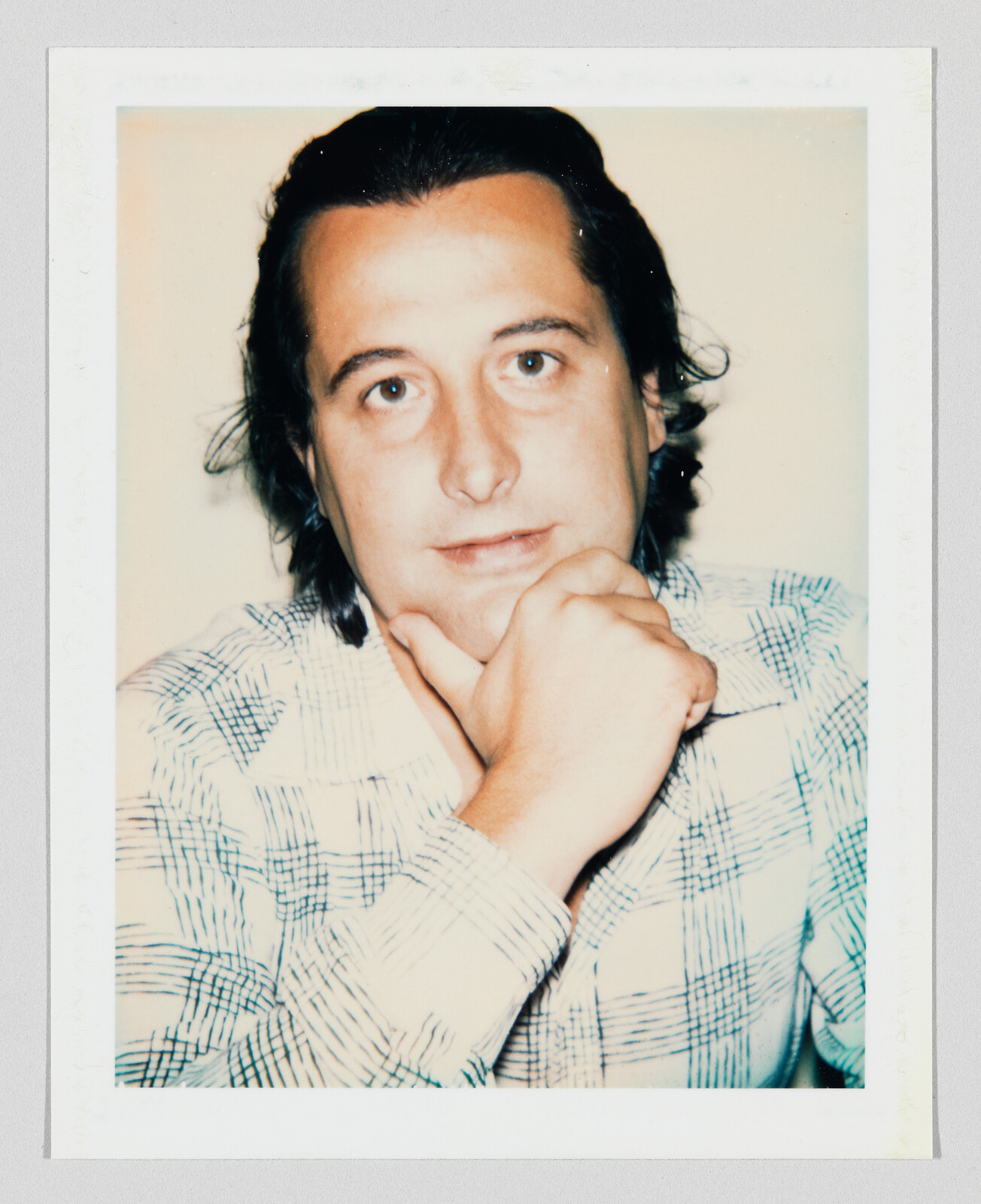 A man with dark hair rests his chin on his hand while looking at the camera.