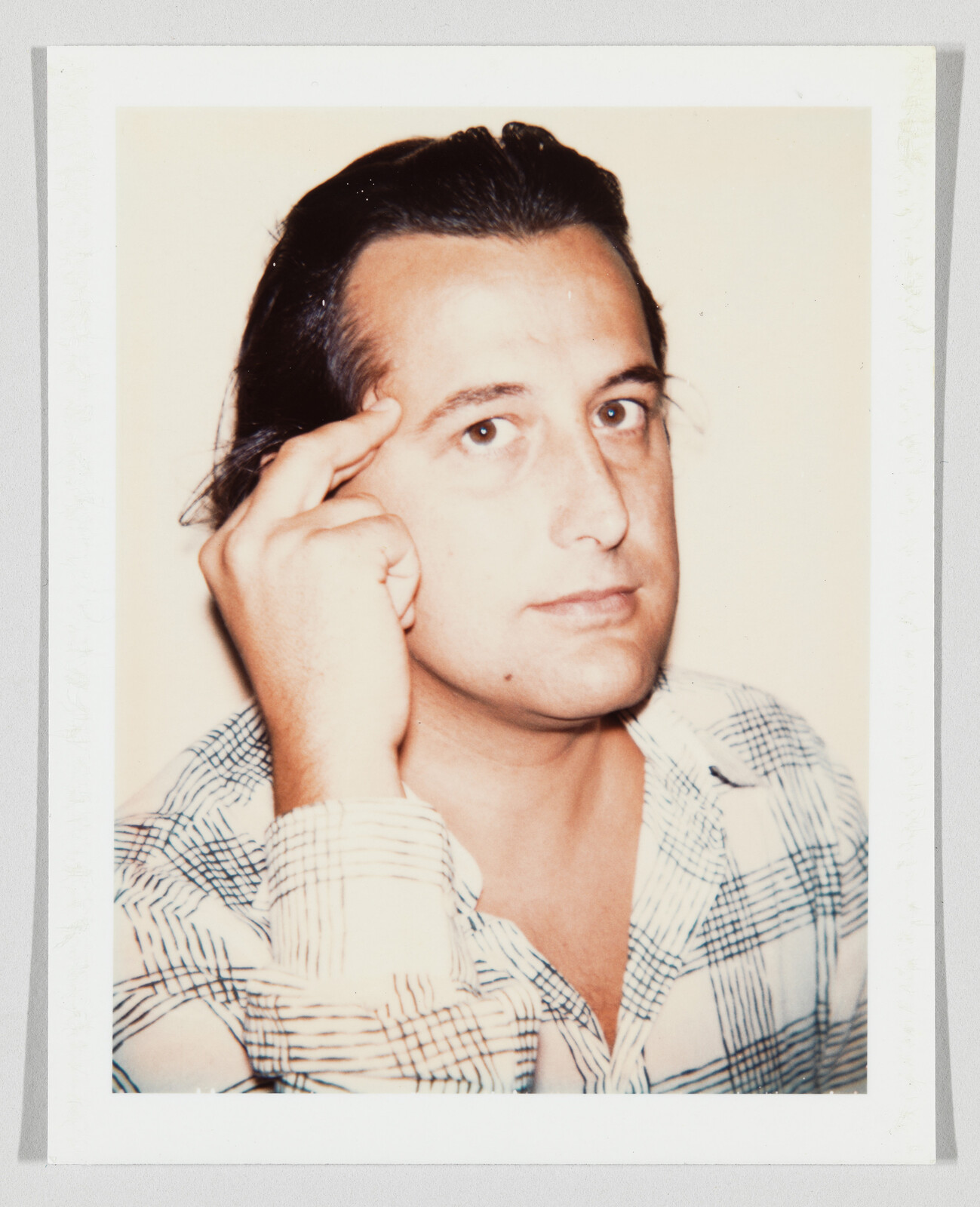 Man with dark hair pointing at his temple while looking toward the camera.