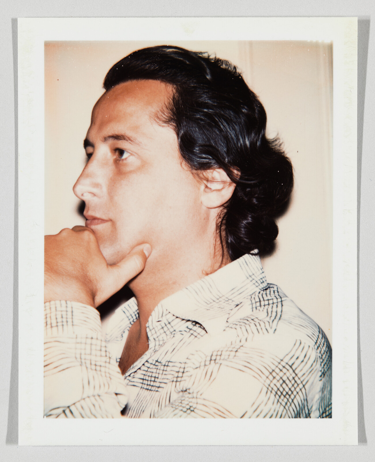 Man with dark hair in a patterned shirt rests his chin on his hand, looking thoughtful.