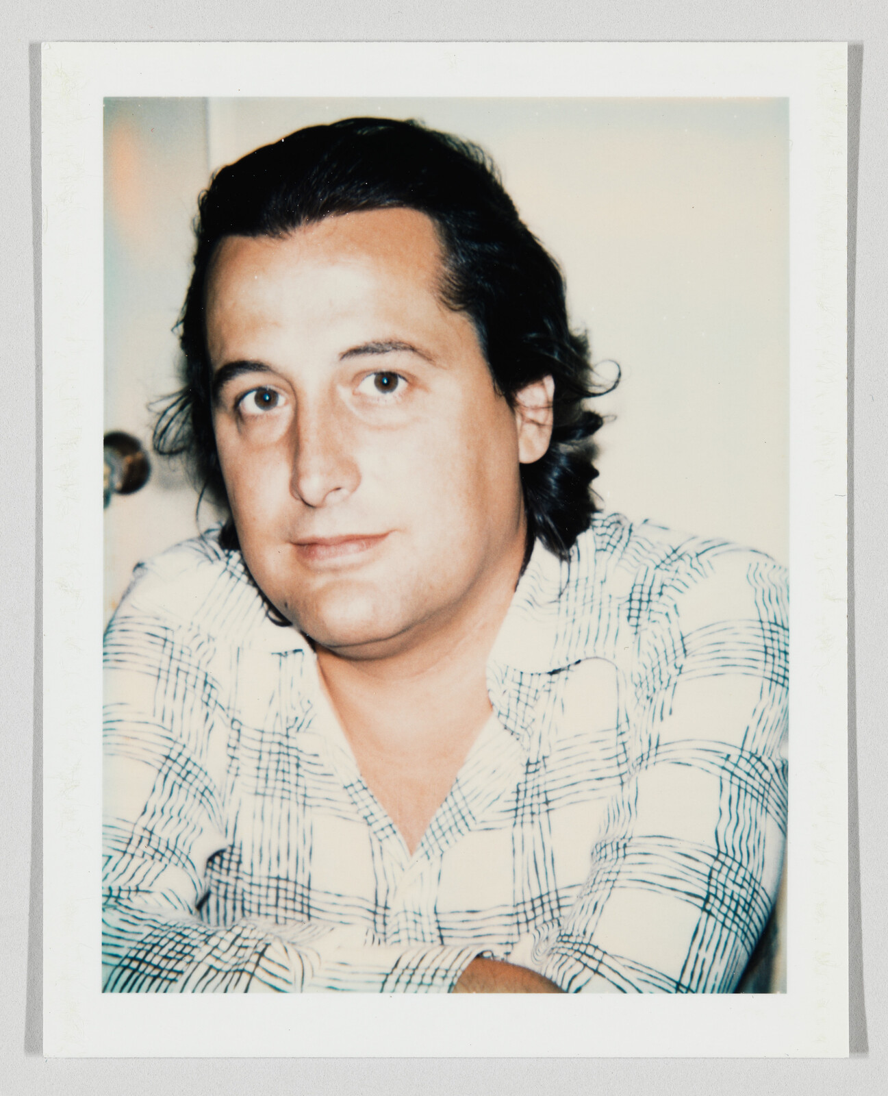 A man with dark hair wearing a checked shirt looks directly at the camera.