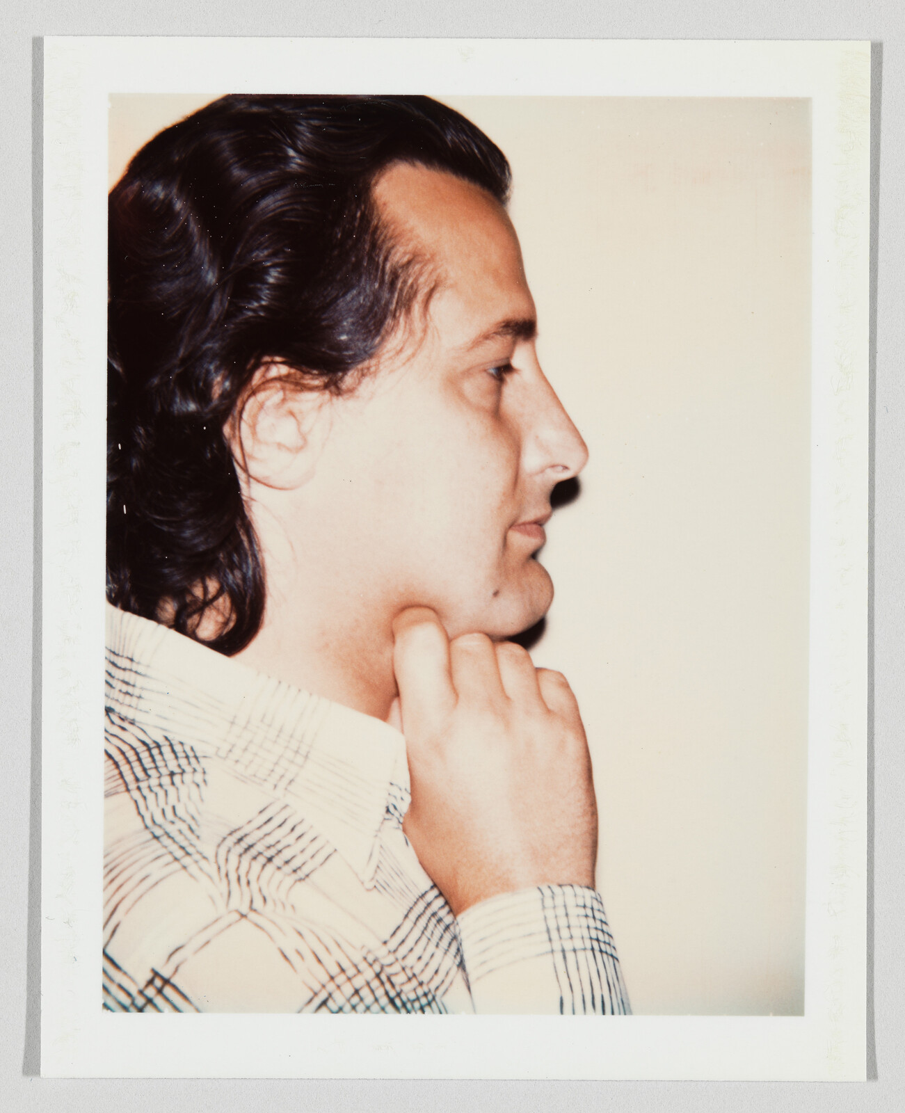 A man in profile rests his chin on his hand while looking ahead.