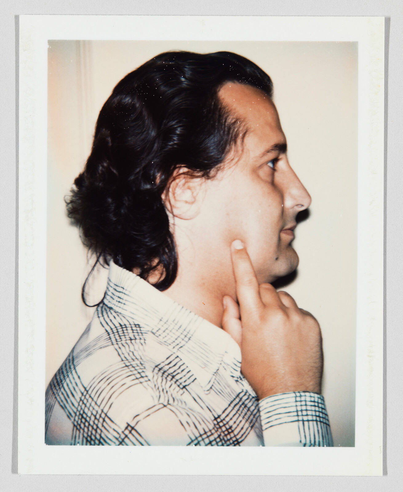 A man in a patterned shirt points with his finger to his jaw while facing right.