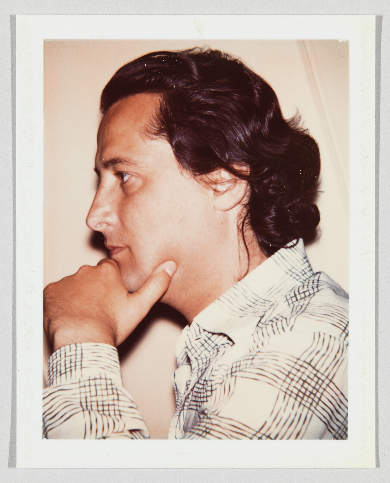 A man in profile rests his chin on his hand while wearing a patterned shirt.
