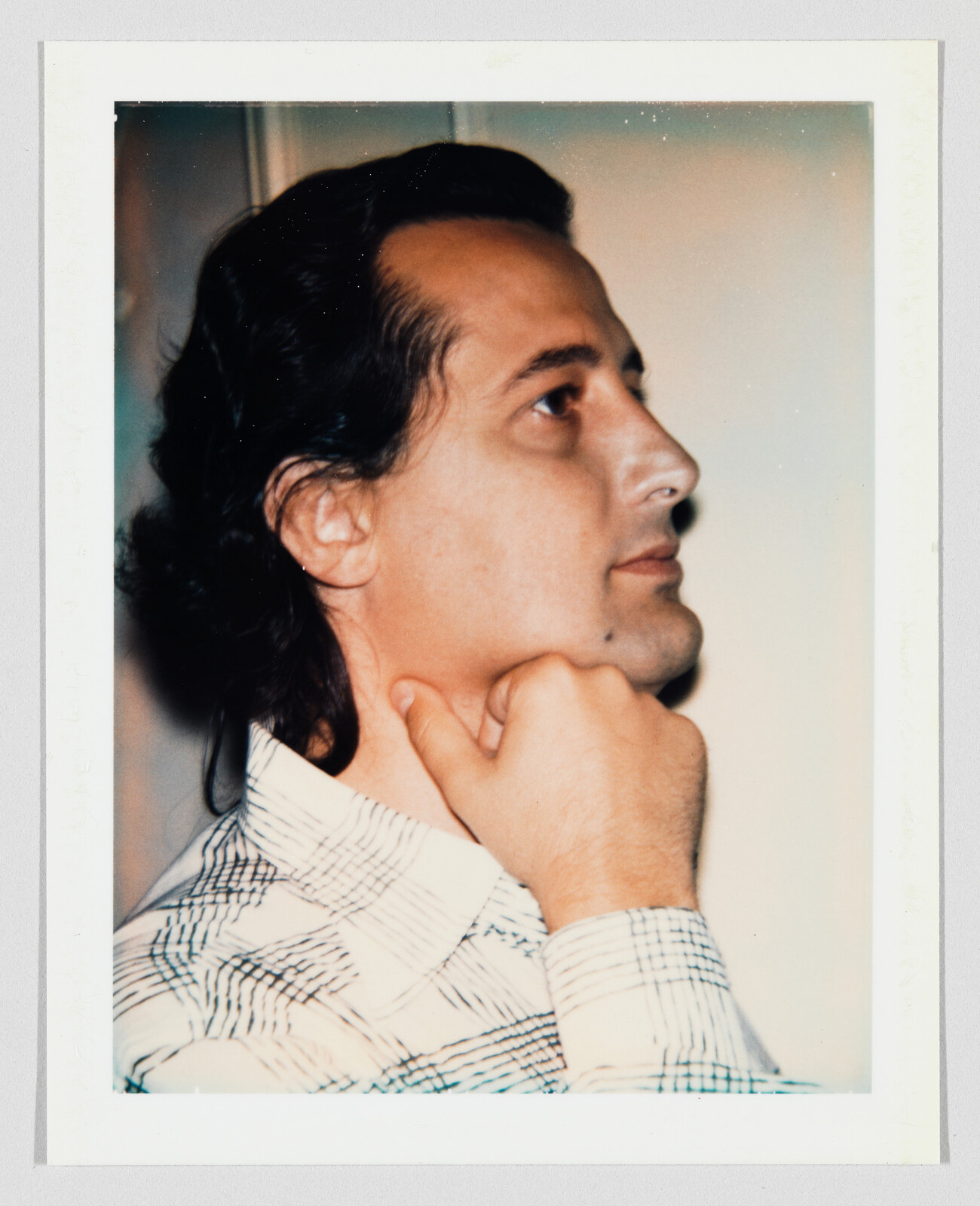 Man with dark hair looks to the side, resting his chin on his hand, wearing a patterned shirt.