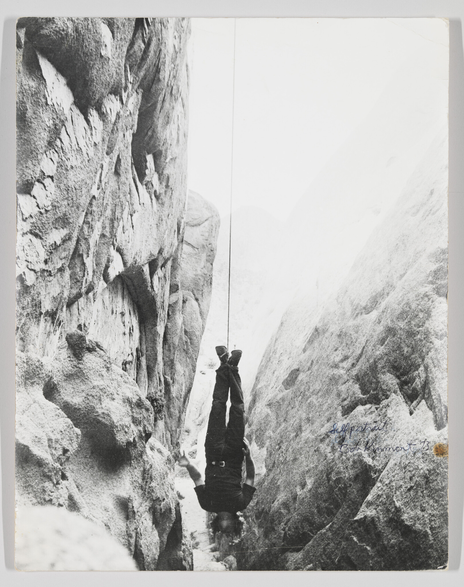 A person hangs upside down suspended by a rope between two steep rock walls.