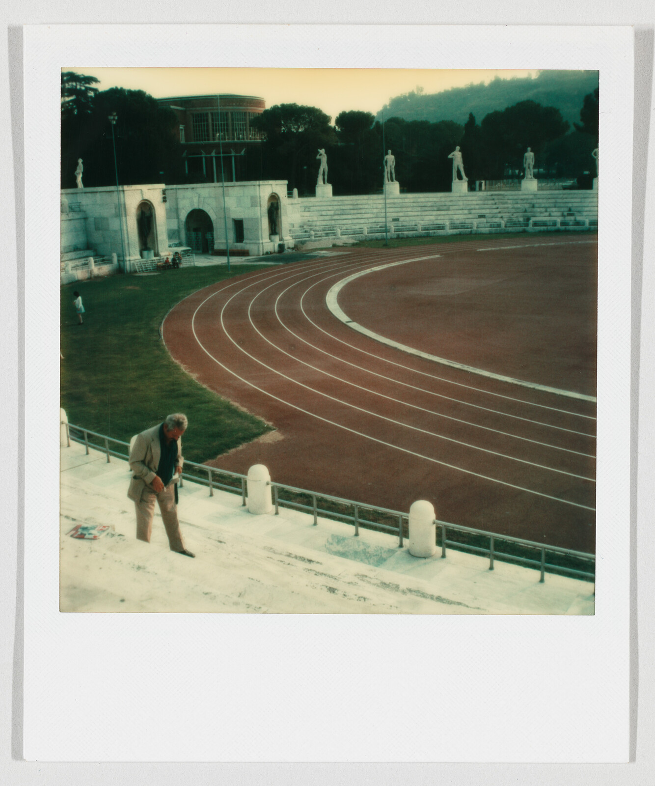 An older man walks up stone stadium steps beside an empty running track.