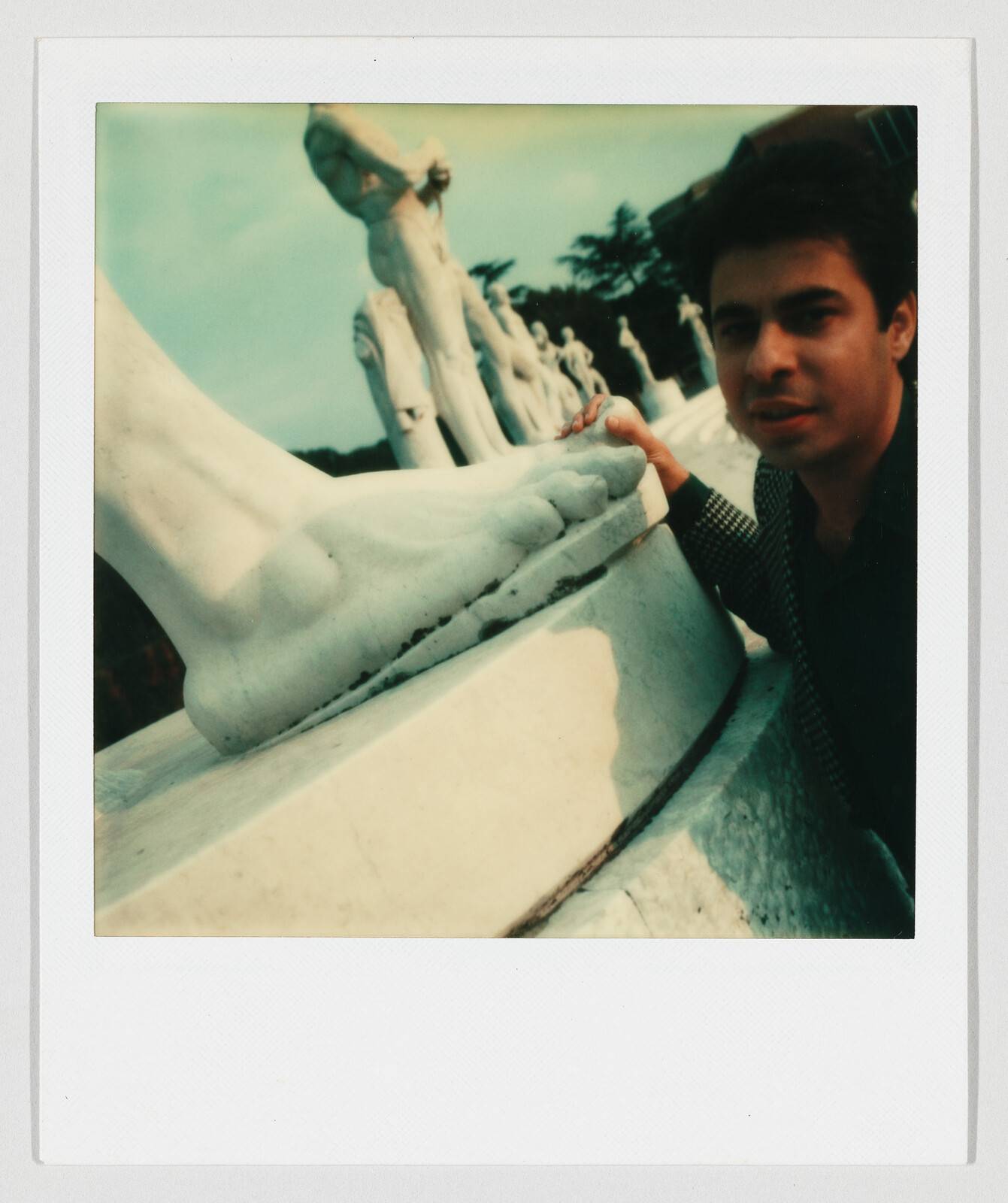 A man crouches beside a row of marble statues, touching the large statue's foot.