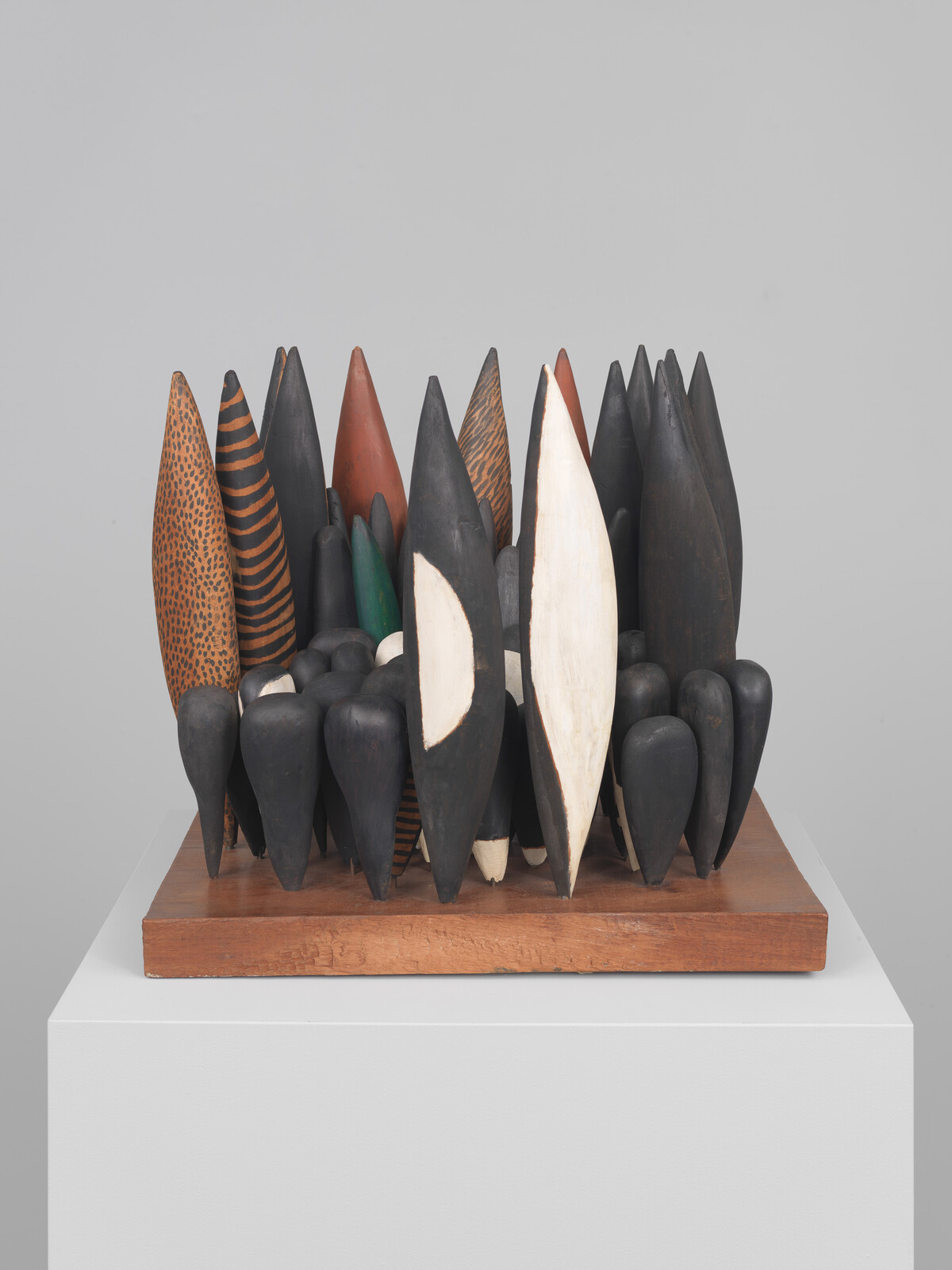 Cluster of tall carved wooden pod shapes in black, white, brown, and striped patterns on a wooden base.