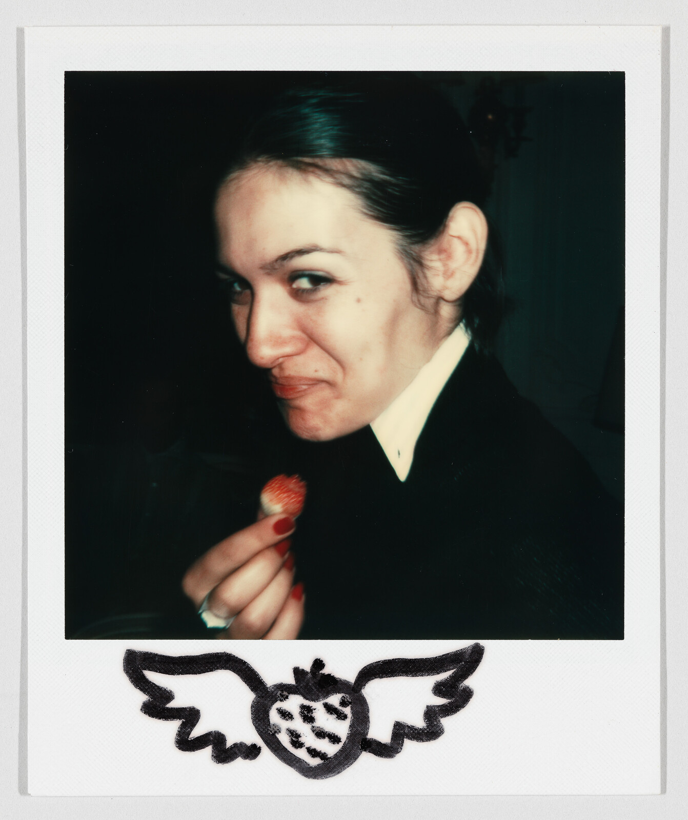 A woman holding a strawberry and smirking at the camera.