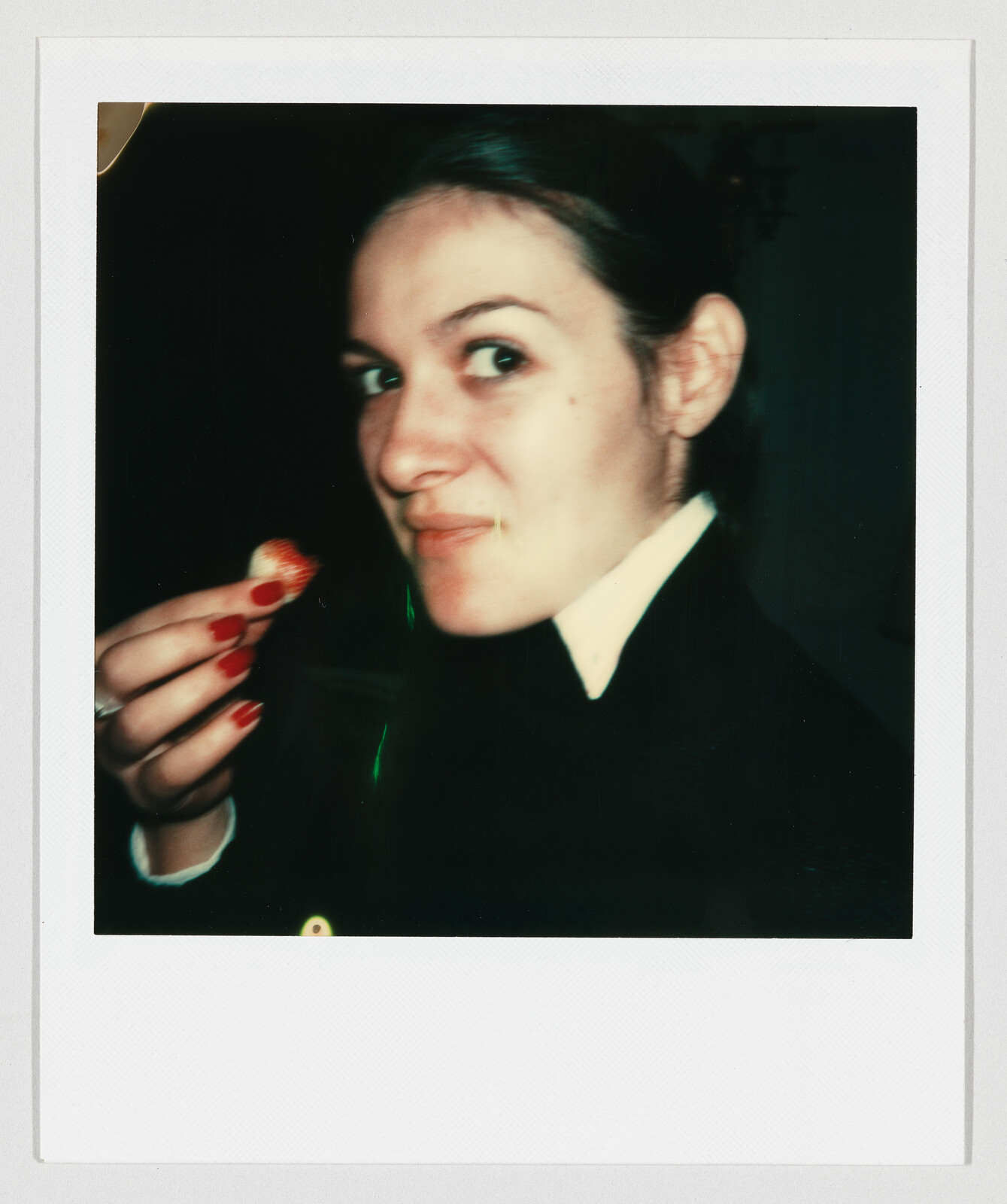 Young woman with red nails eating a strawberry while looking toward the camera with a slight smile.