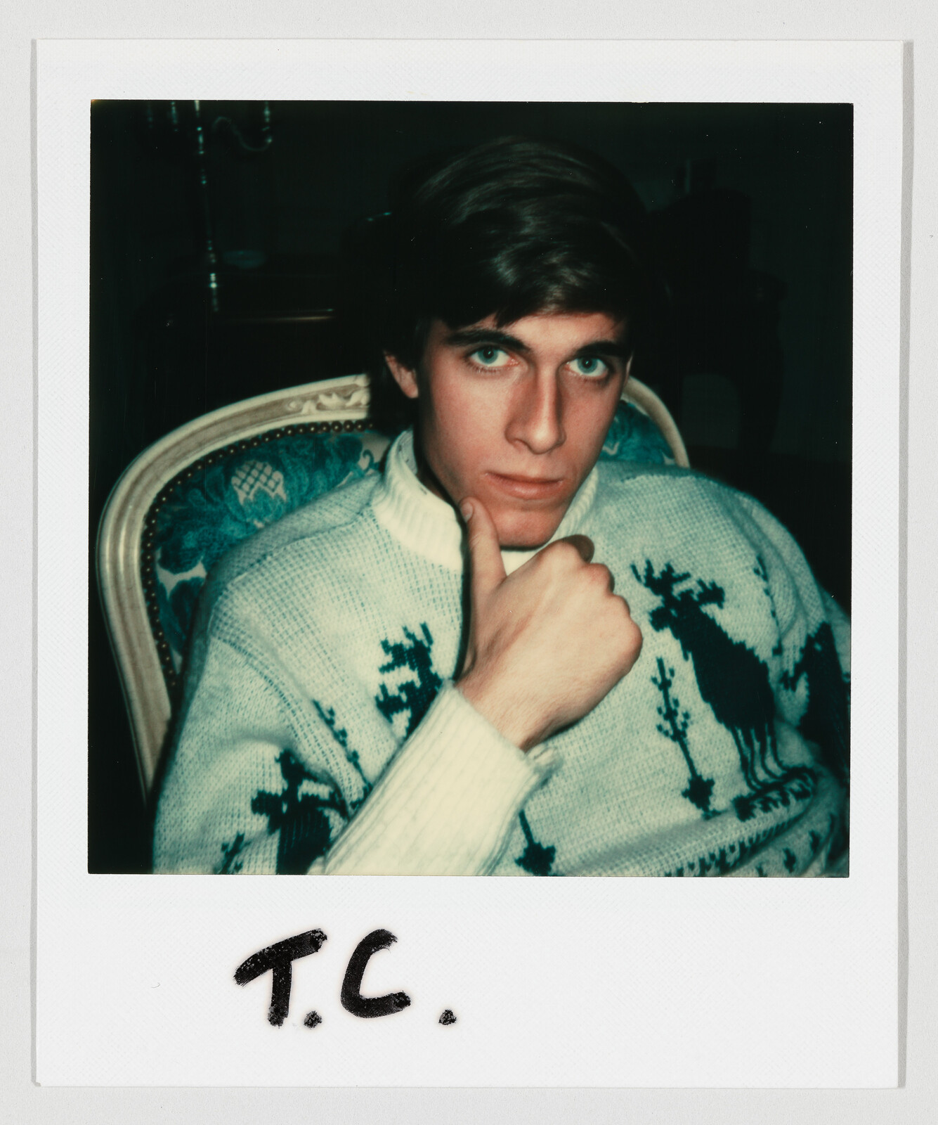 Young man in a patterned sweater sits with chin resting on hand, handwritten initials 'T.C.' below.