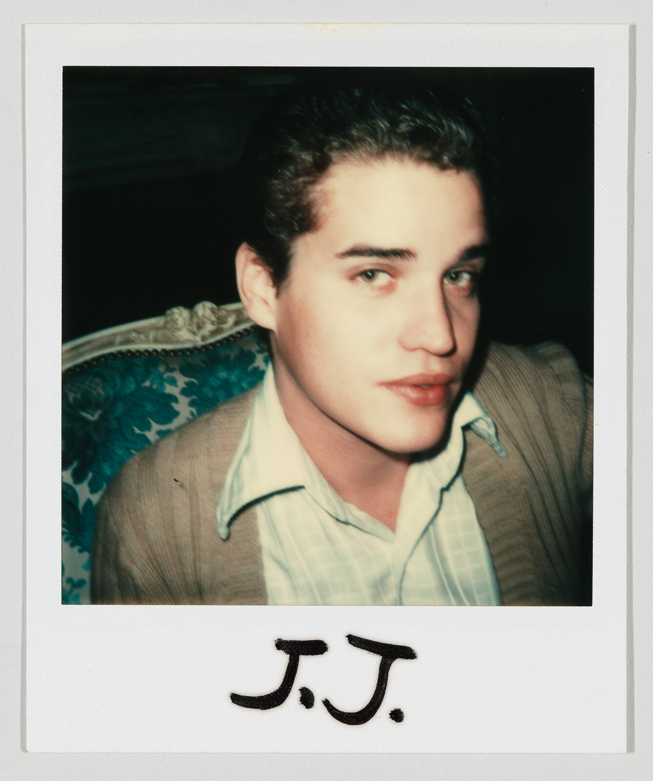 Young man in a cardigan looks toward the camera while a Polaroid label reads "J.J.".