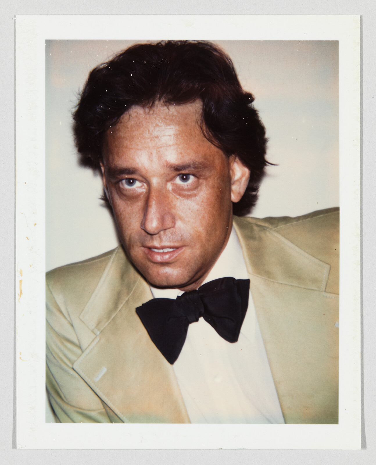 A man in a beige tuxedo jacket and black bow tie gazes slightly off camera.