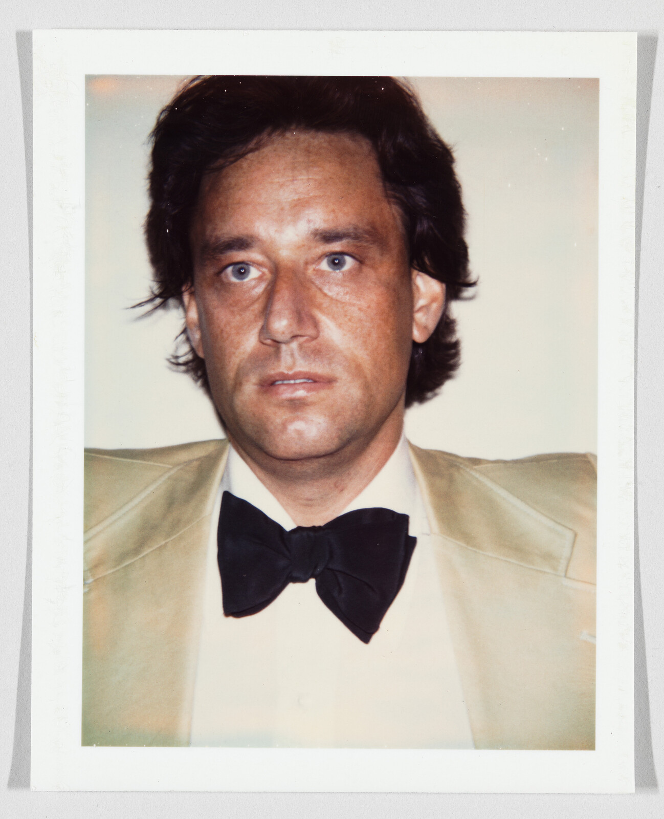 Man in a tan suit jacket and black bow tie looking straight at the camera.