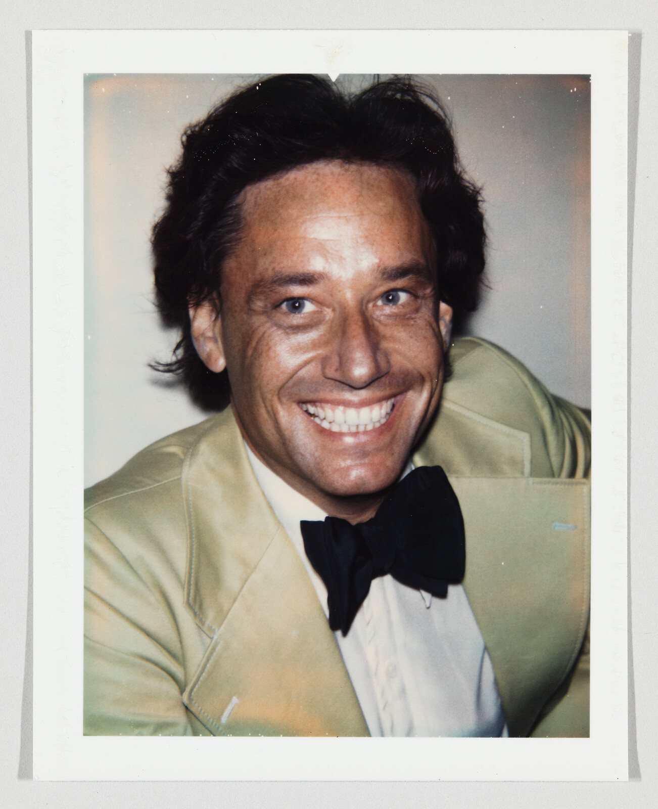 Smiling man wearing a tan suit jacket and black bow tie in a close-up portrait.