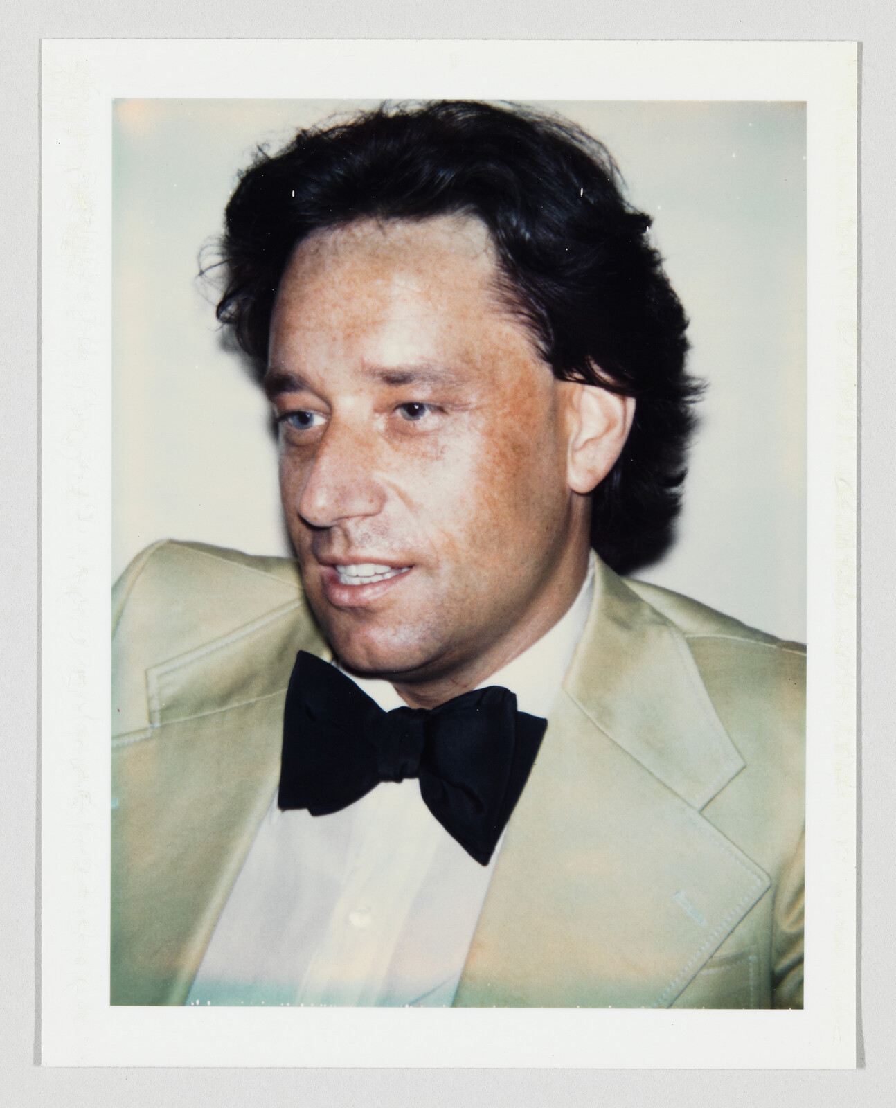 A man in a cream tuxedo jacket and black bow tie looking slightly to his right.