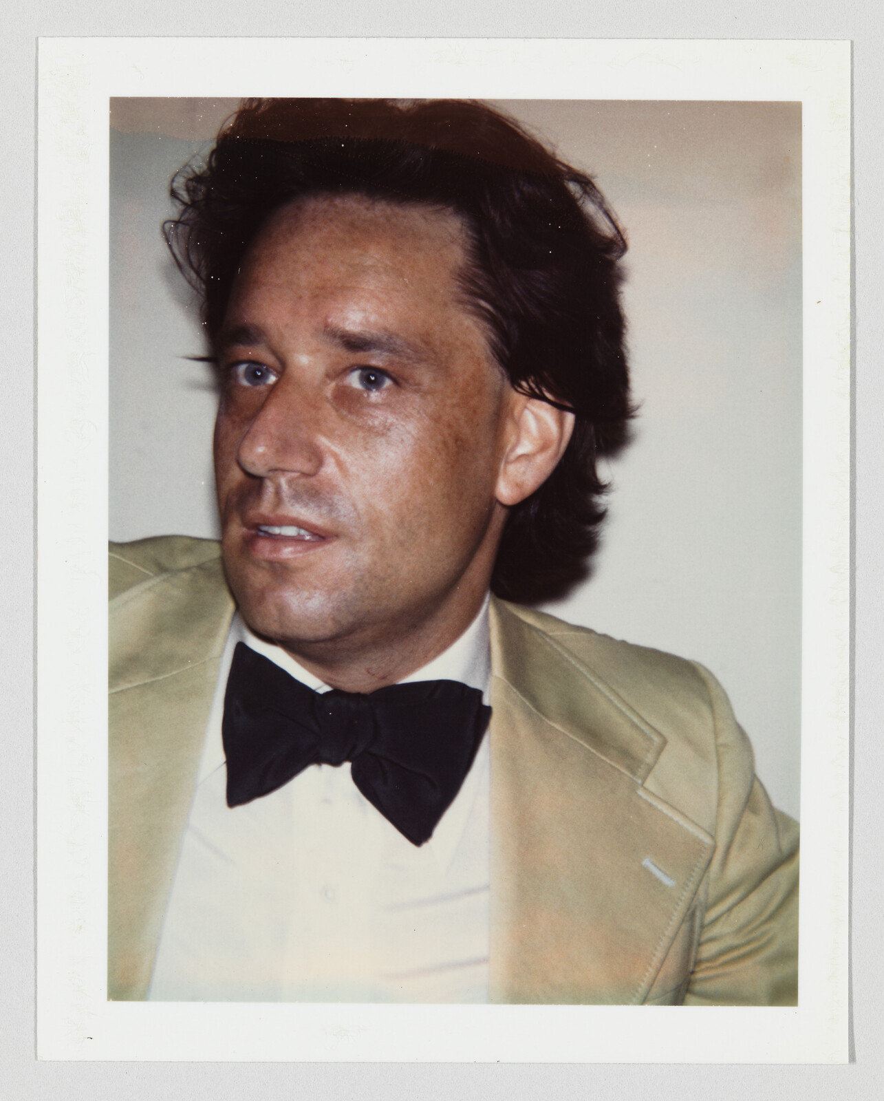 Man wearing a tan suit jacket and black bow tie looking slightly to the left.