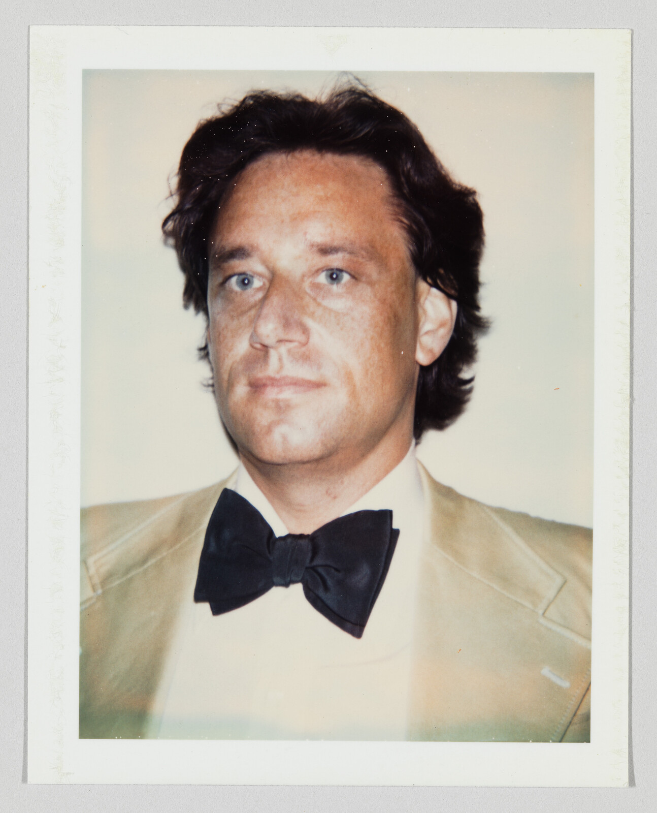 Man wearing a beige suit jacket and a black bow tie looking slightly off camera.