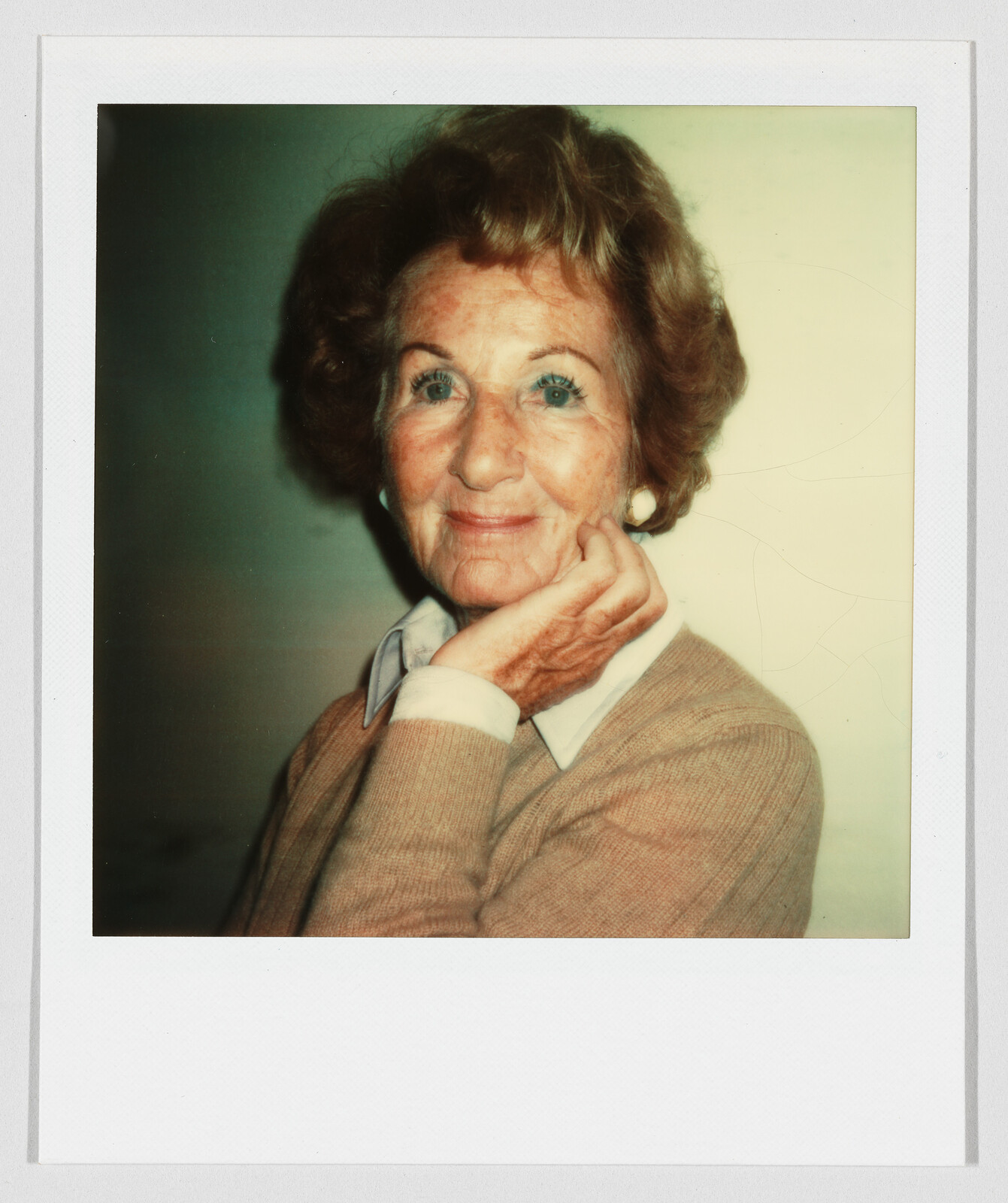 Elderly woman with short curly hair smiles gently while resting her chin on her hand.