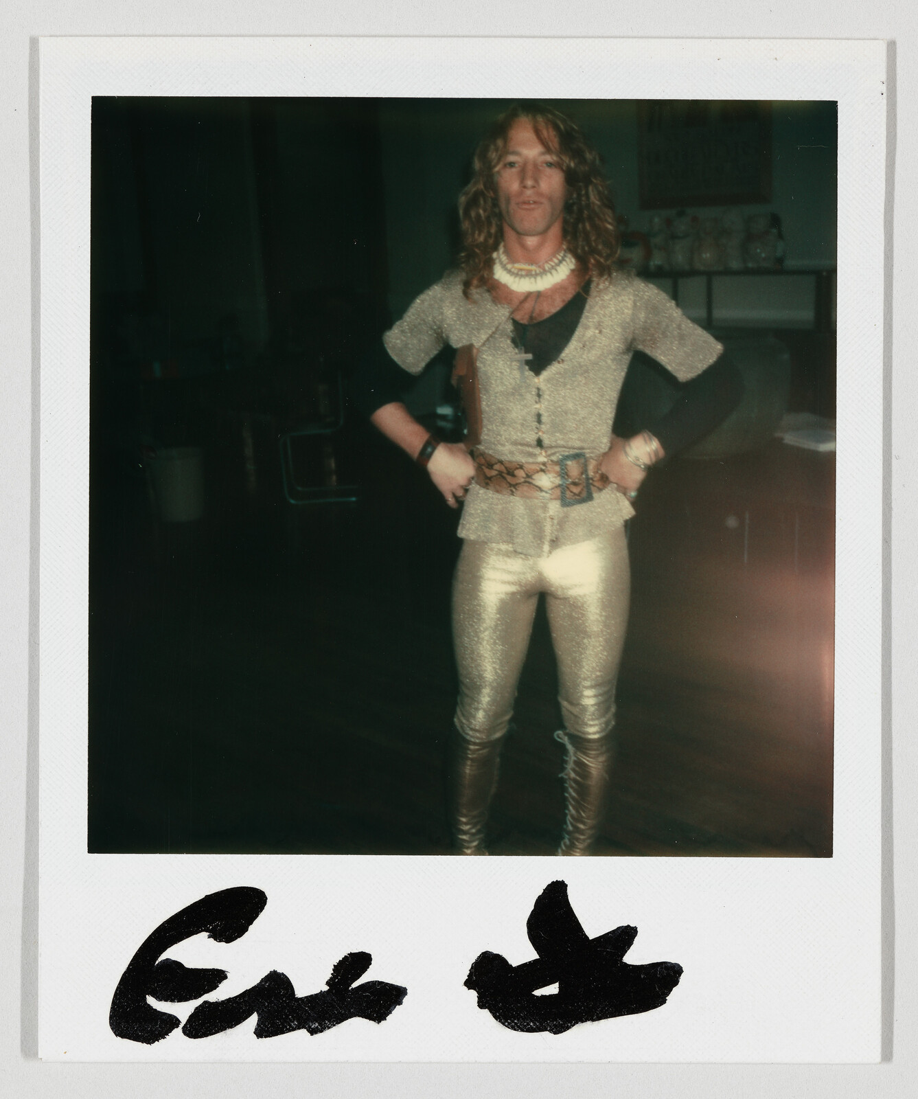 Person wearing sparkly gold top and leggings with hands on hips in a dim room.