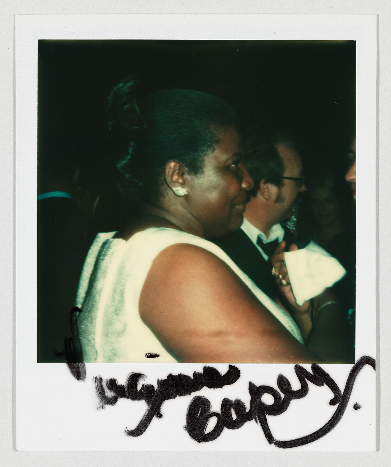 A woman in a white sleeveless dress converses with others at a formal evening event.