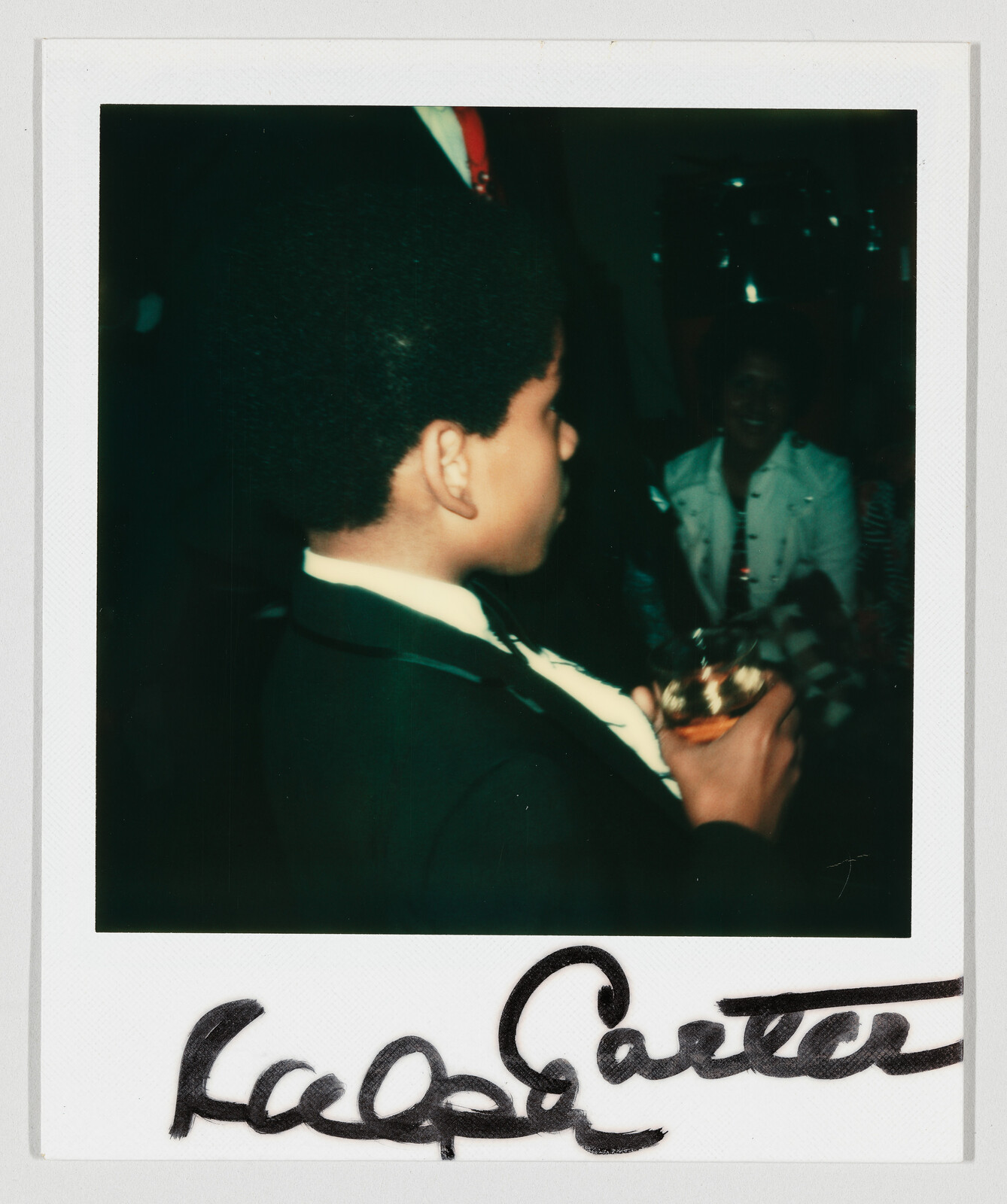 Young boy in a suit holding a drink and looking to the right at a party.