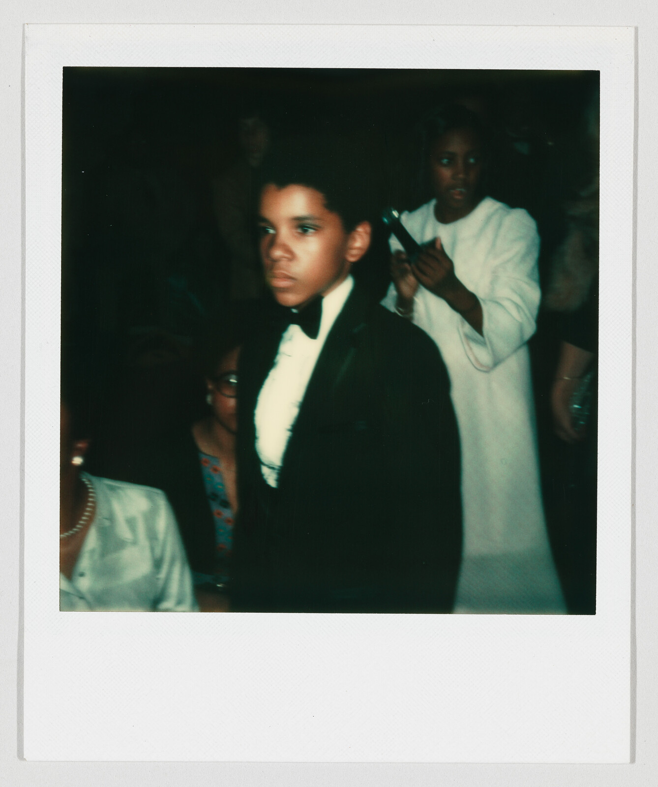 Young boy in a tuxedo walks forward while guests clap and watch attentively.