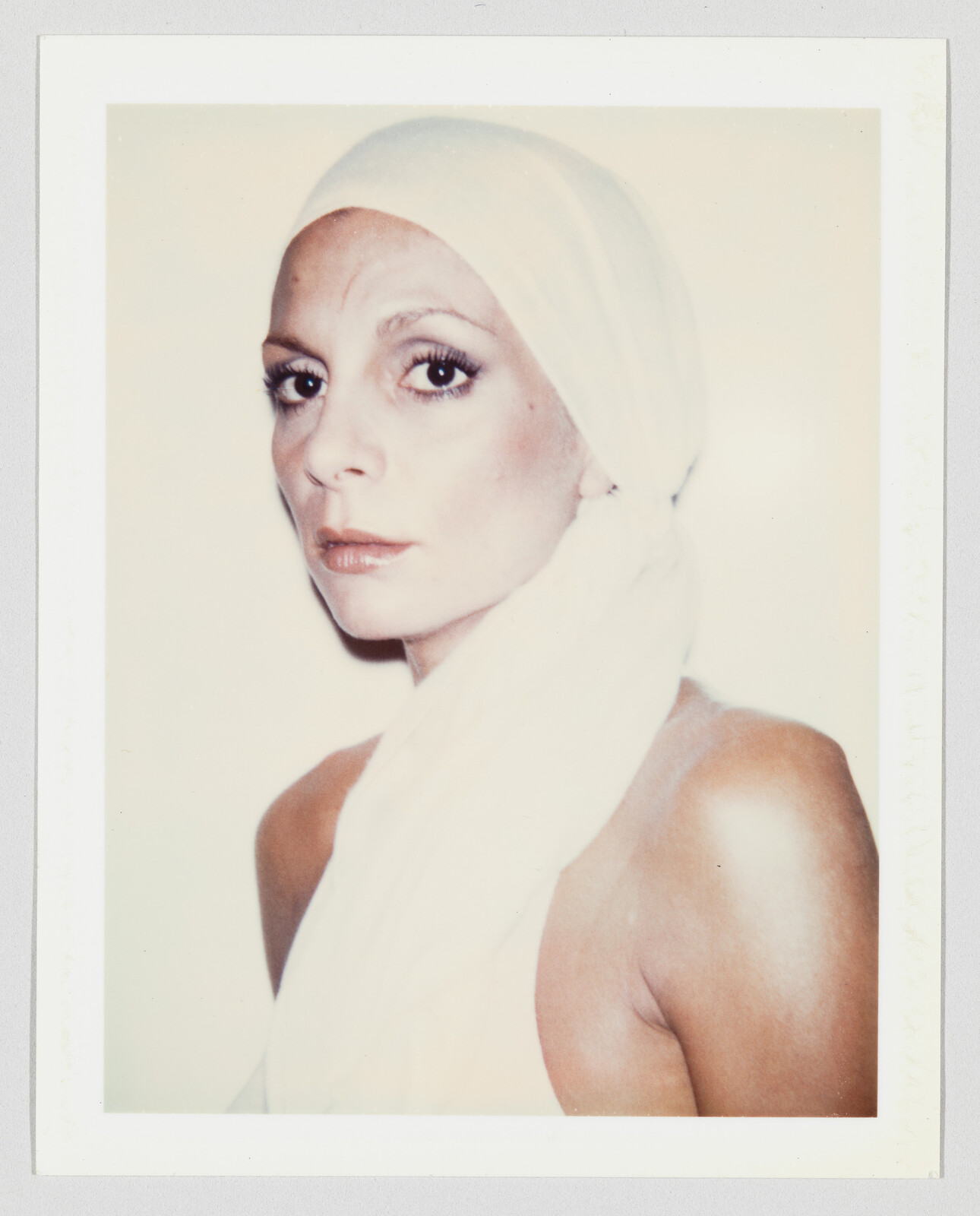 Person with bare shoulders wearing a white headscarf, looking slightly to the side with a neutral expression.