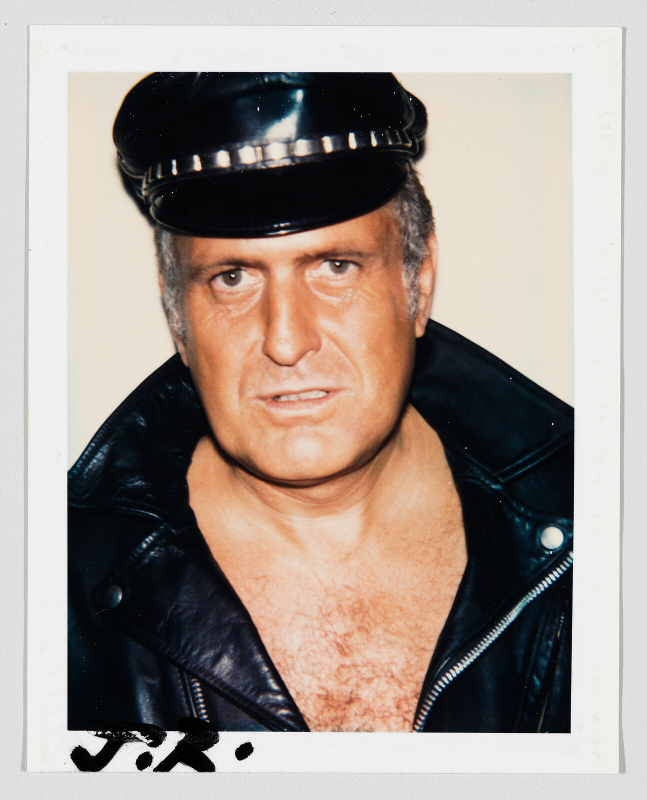 Middle-aged man wearing a leather biker cap and jacket stares directly at the camera.