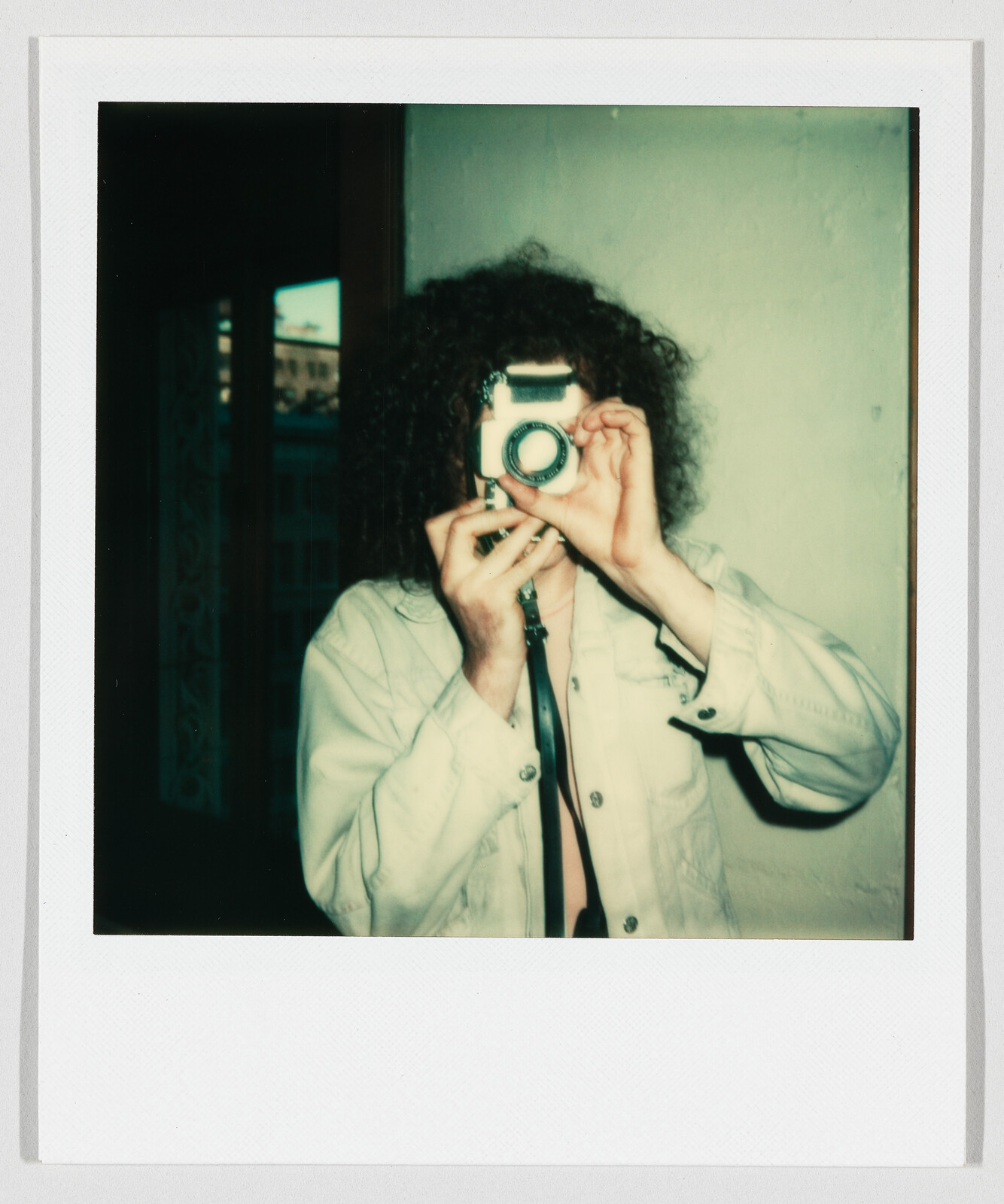 Person with curly hair holds a vintage camera up to their face and takes a picture.