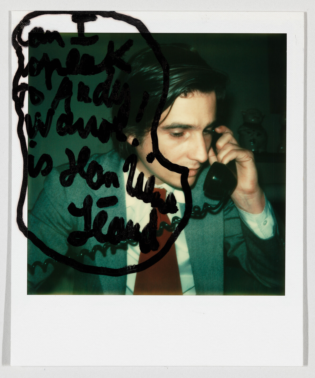 Young man in a suit talks on a corded phone while black marker scribbles partially cover the image.