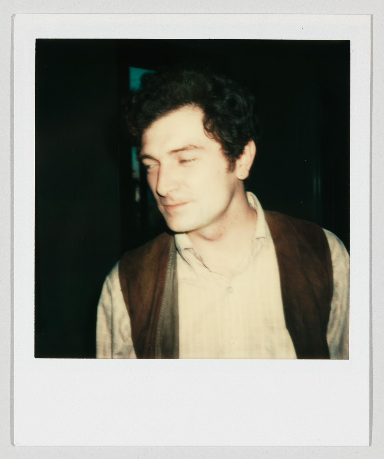 A young man in a vest and button-up shirt looks off to the left with a faint smile.