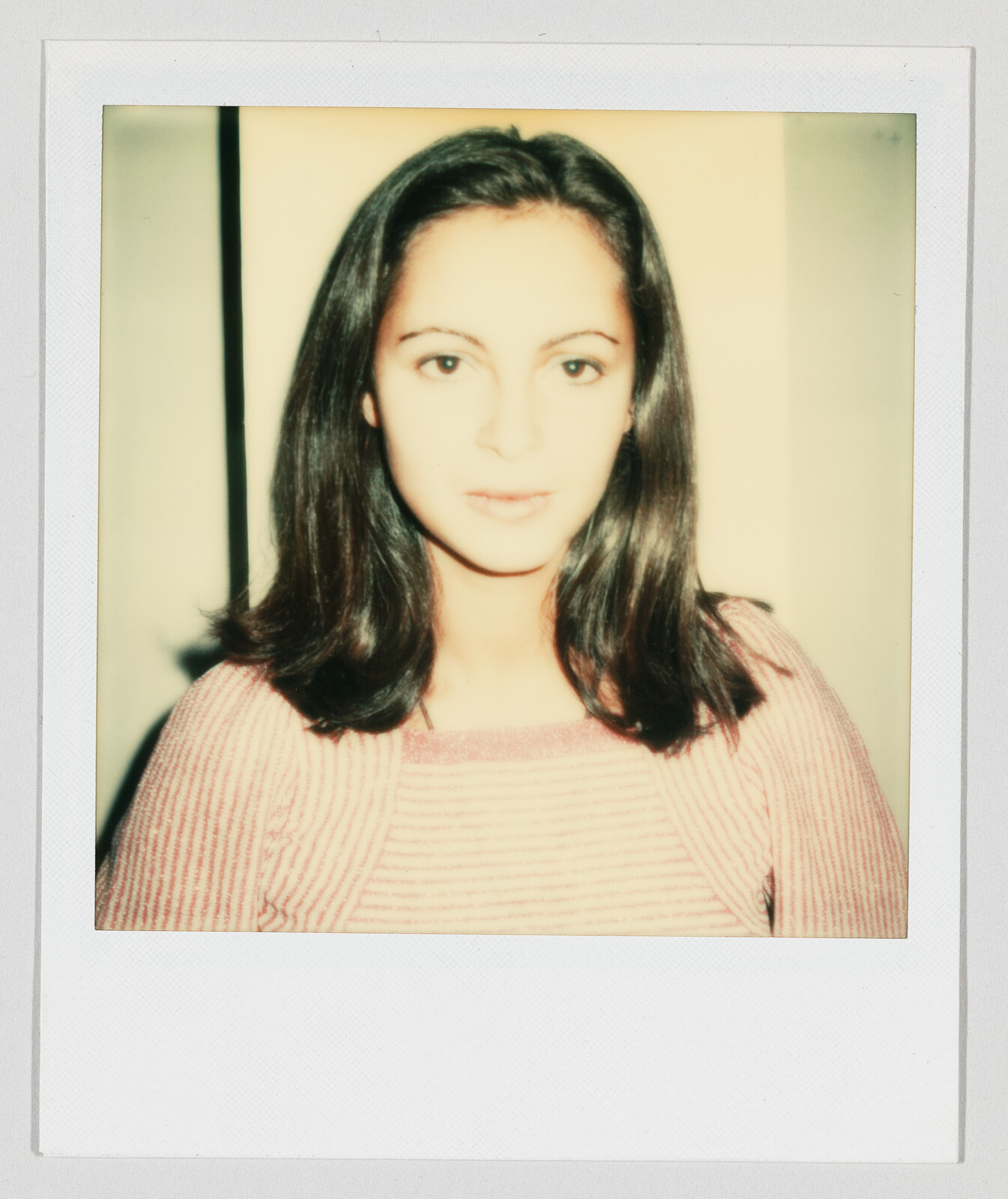 Young woman with shoulder-length dark hair looking directly at the camera wearing a pink striped sweater.