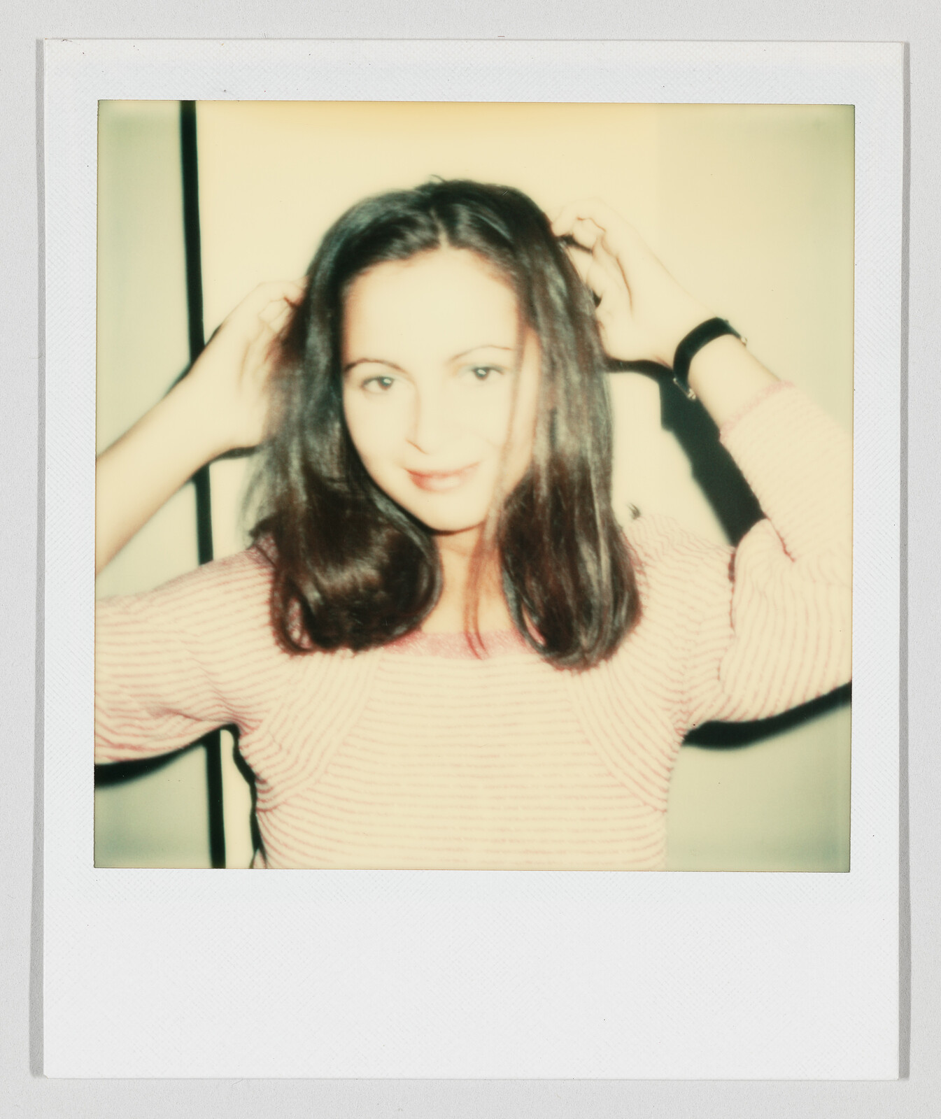 Young woman with shoulder-length dark hair adjusts her hair while smiling at the camera.