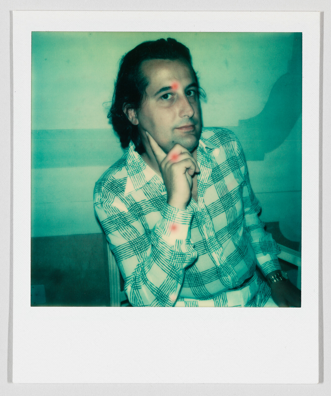 Man in a checkered shirt poses with his hand on his chin, looking toward the camera.