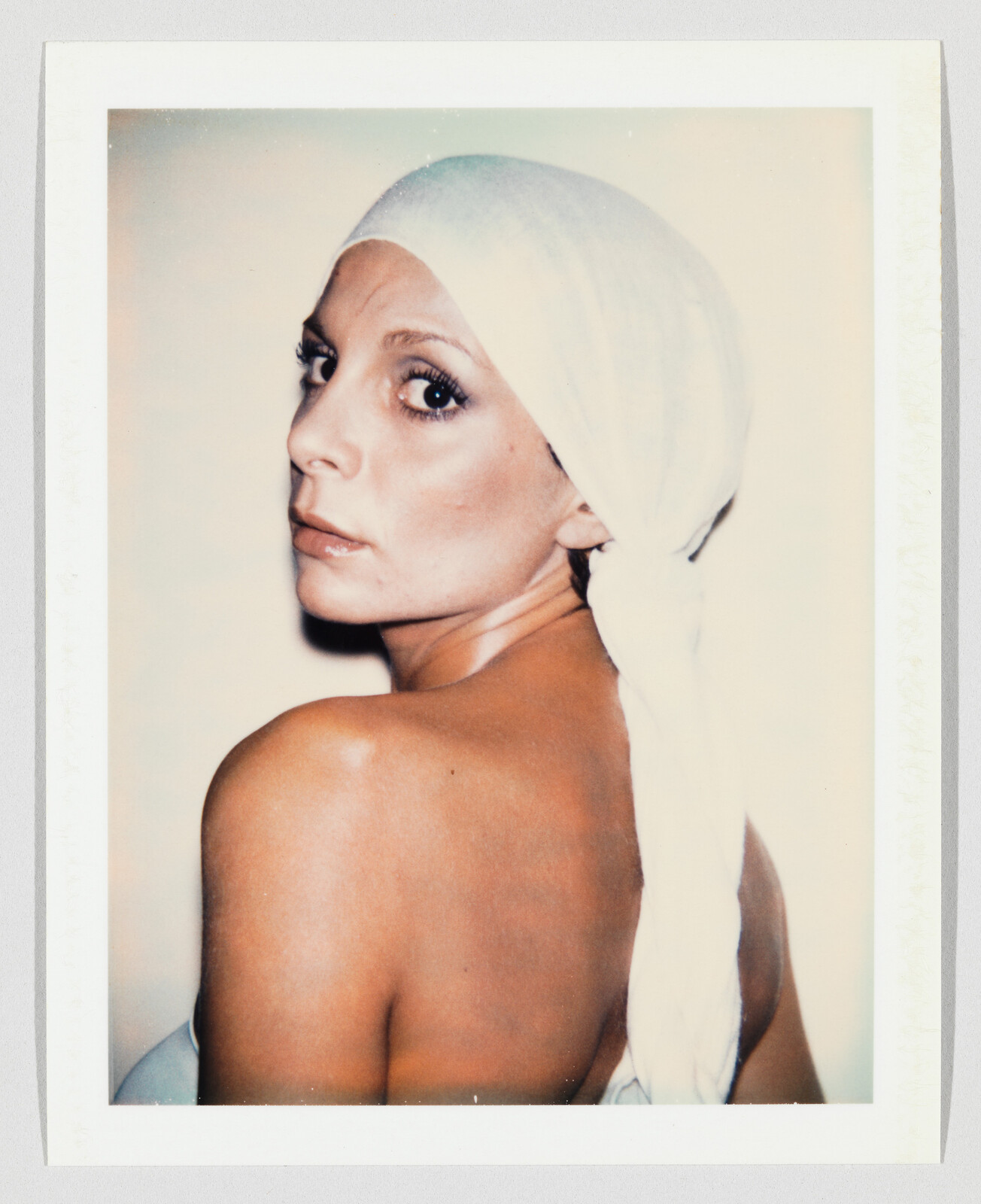 A woman with a white headscarf looks over her shoulder, showing her bare back.