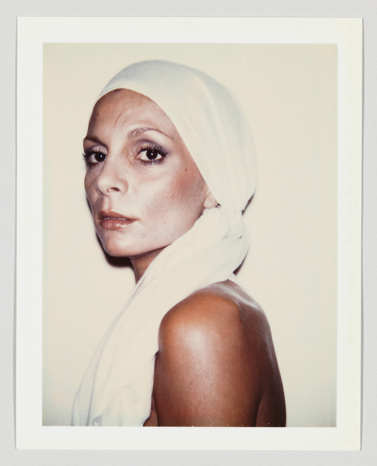 Woman in a white headscarf looks over her shoulder with a calm, serious expression.