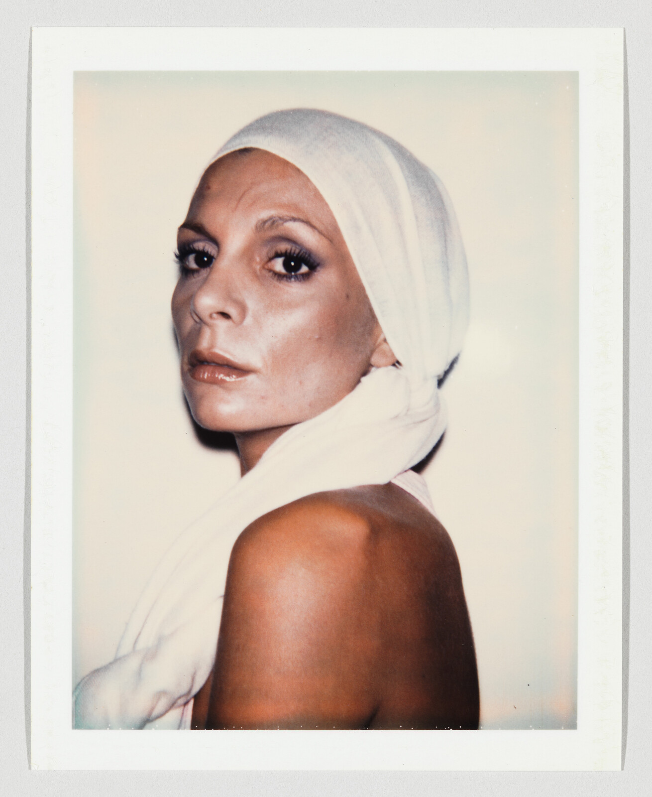 A woman wearing a white headscarf looks over her shoulder with a serious expression.