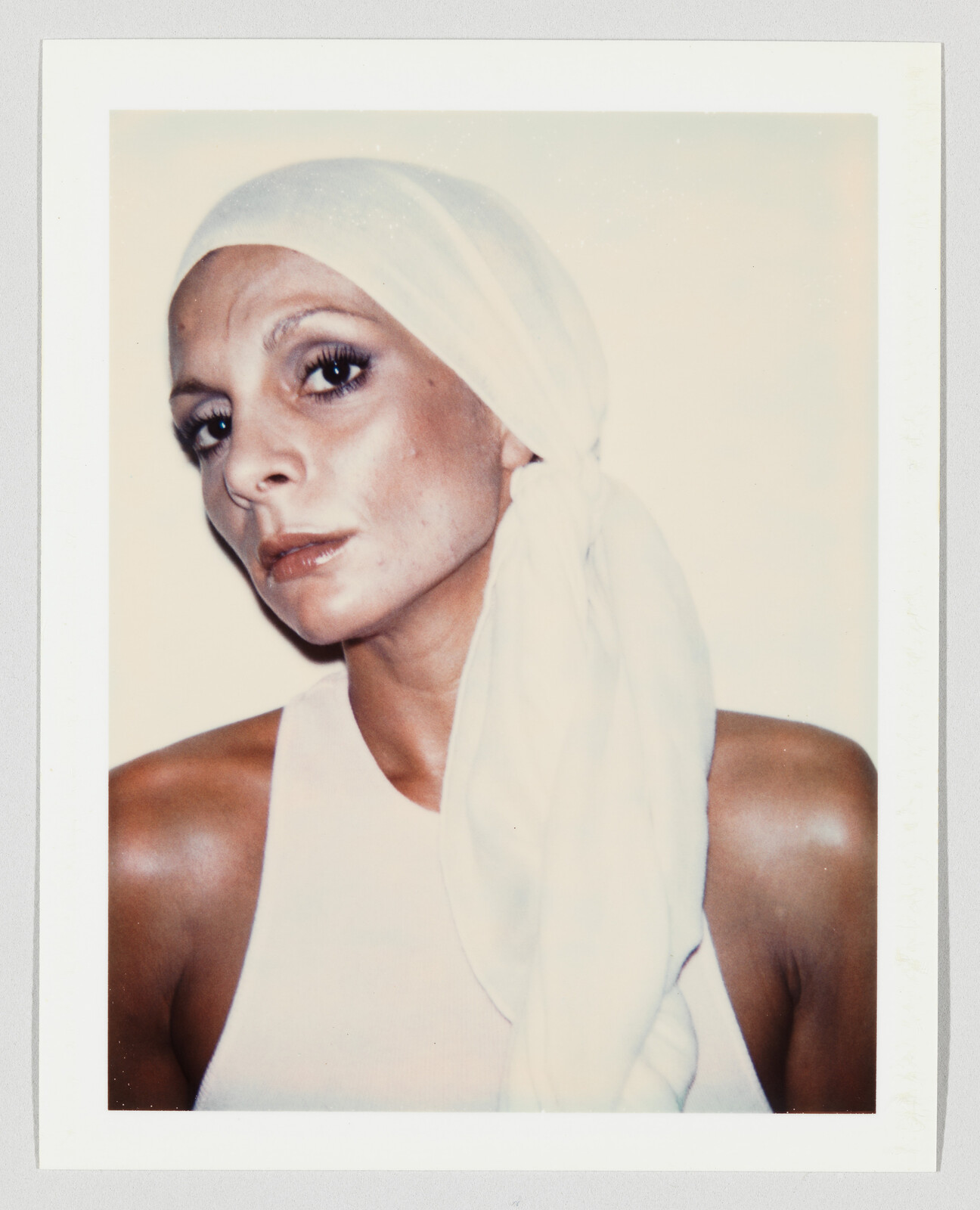 Woman wearing a white headscarf and tank top looks directly at the camera with a neutral expression.