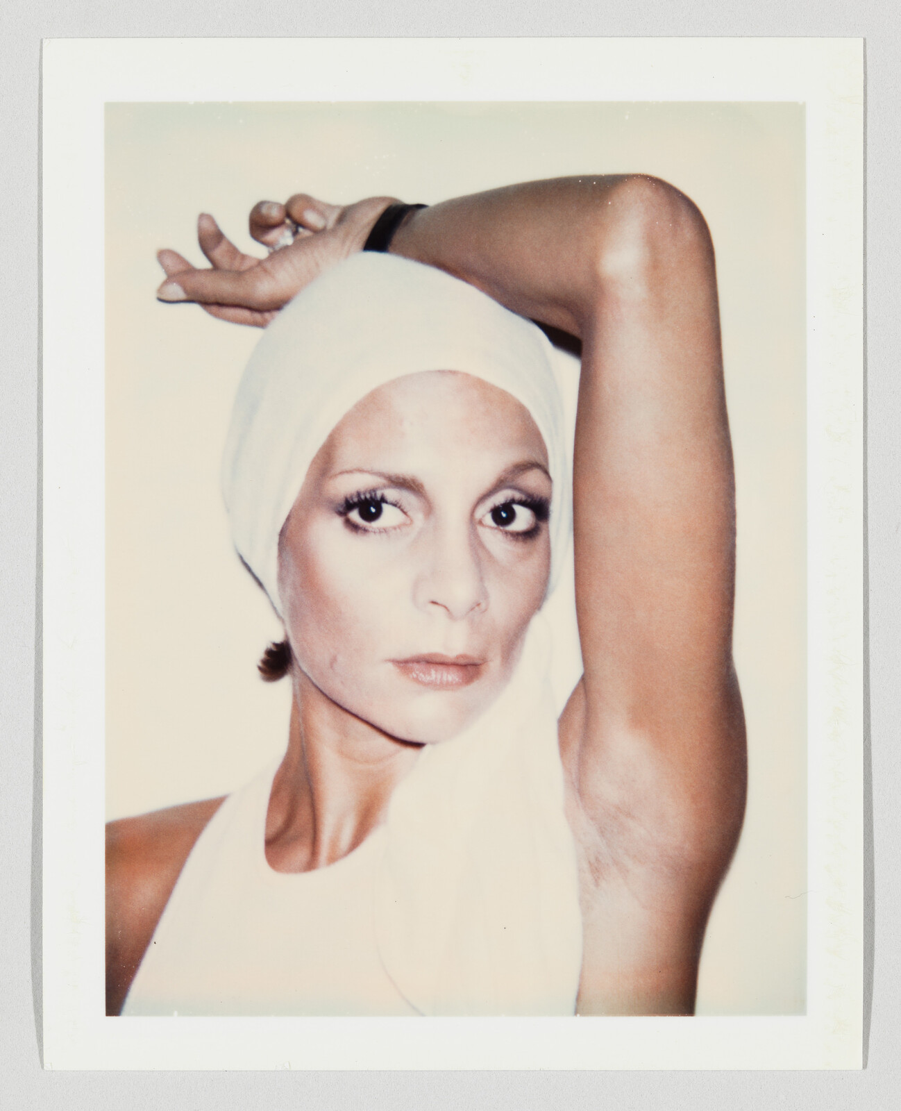 Woman wearing a white headscarf raises one arm while looking slightly to her left.