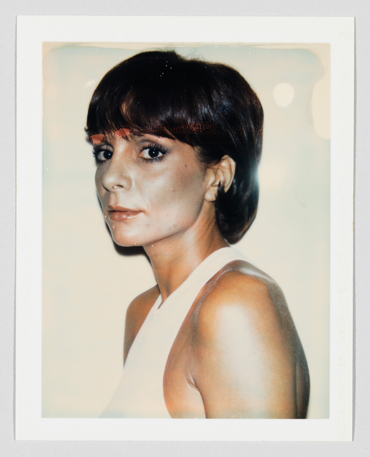 A woman with short dark hair looks over her shoulder with a neutral expression.