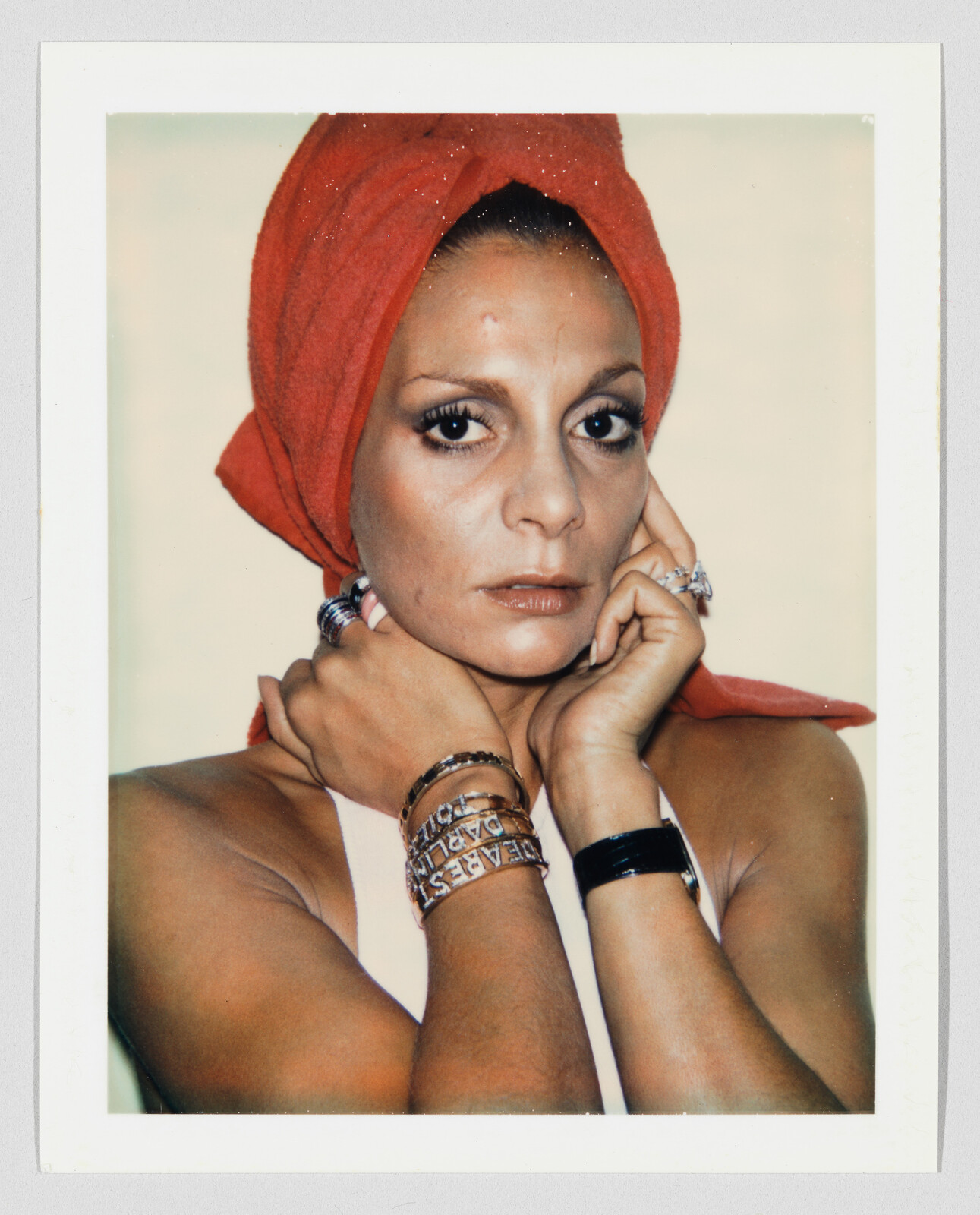 Woman with a red towel wrapped on her head stares at camera, hands touching her face.