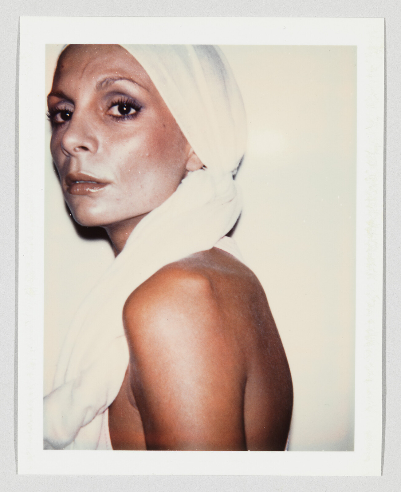 A woman with a towel wrapped around her head looks over her bare shoulder at the camera.