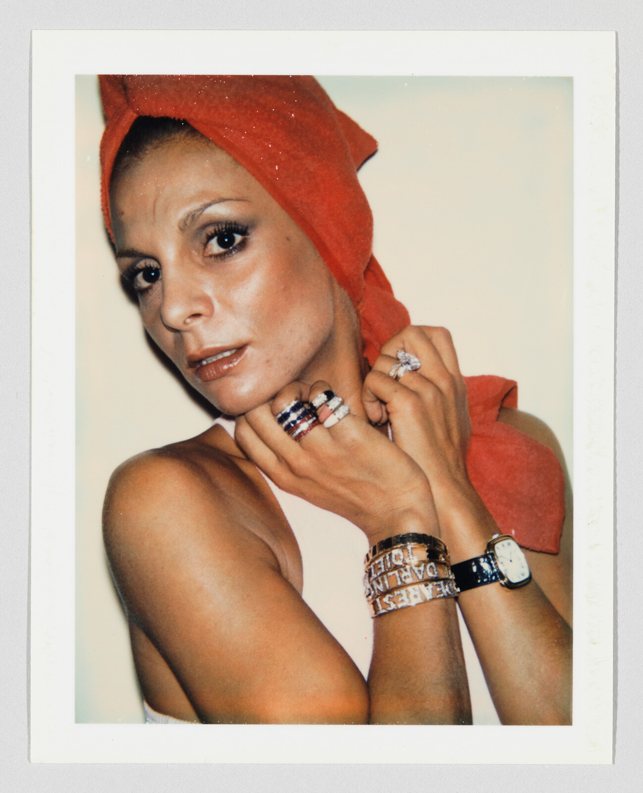 Woman with a red towel wrapped on her head shows multiple rings and bracelets while looking at the camera.