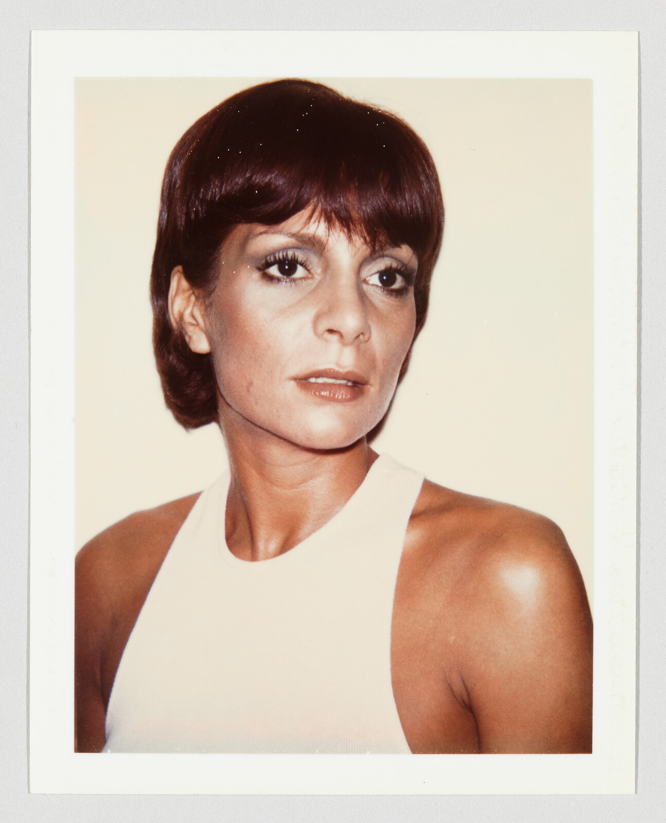 Woman with short brown hair wearing a sleeveless white top and looking slightly to the side.