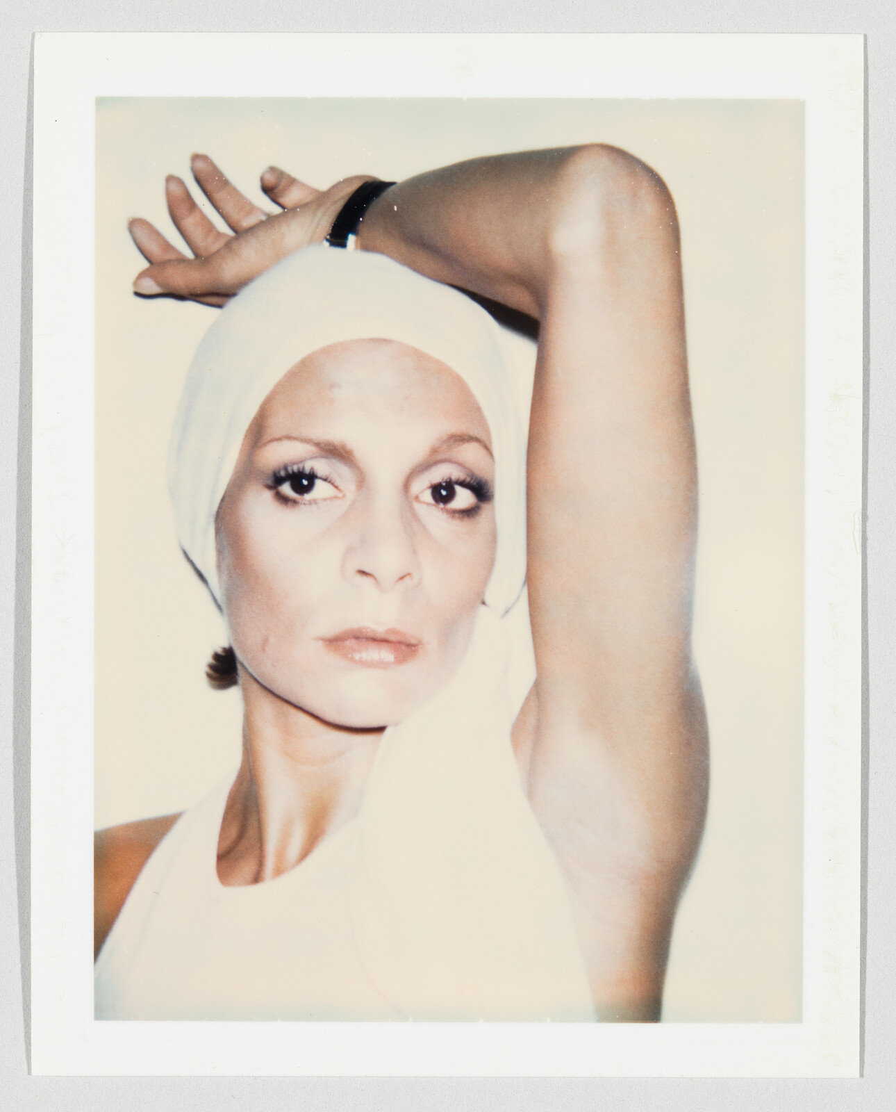 Woman wearing a white headscarf raises one arm above her head while looking directly ahead.