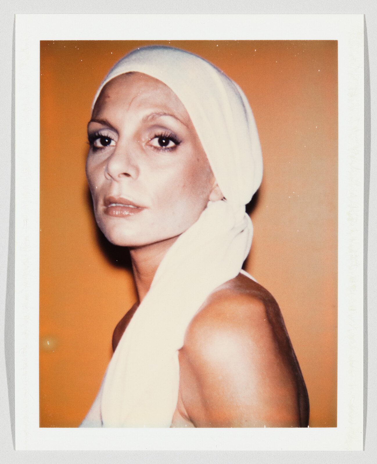 Woman wearing a white headscarf looks over her shoulder against an orange background.