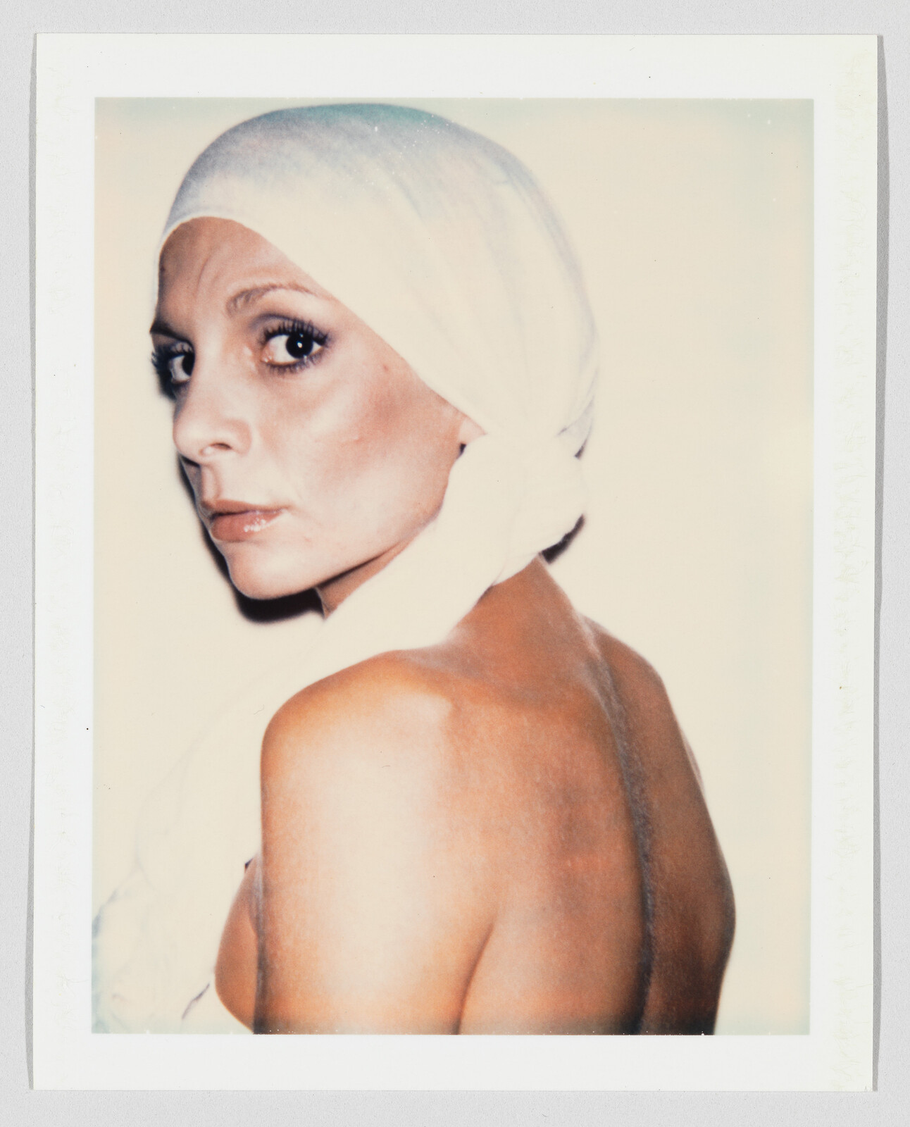 Woman with a white headscarf looks over her shoulder, showing her bare back and intense gaze.