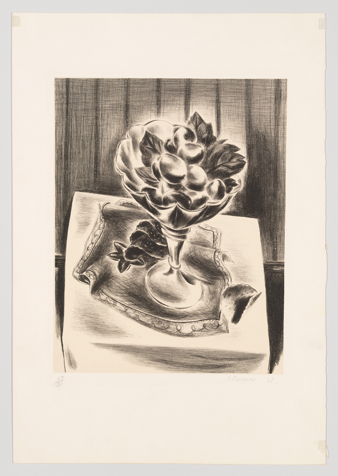 A glass compote filled with fruit sits on a folded cloth atop a small table.