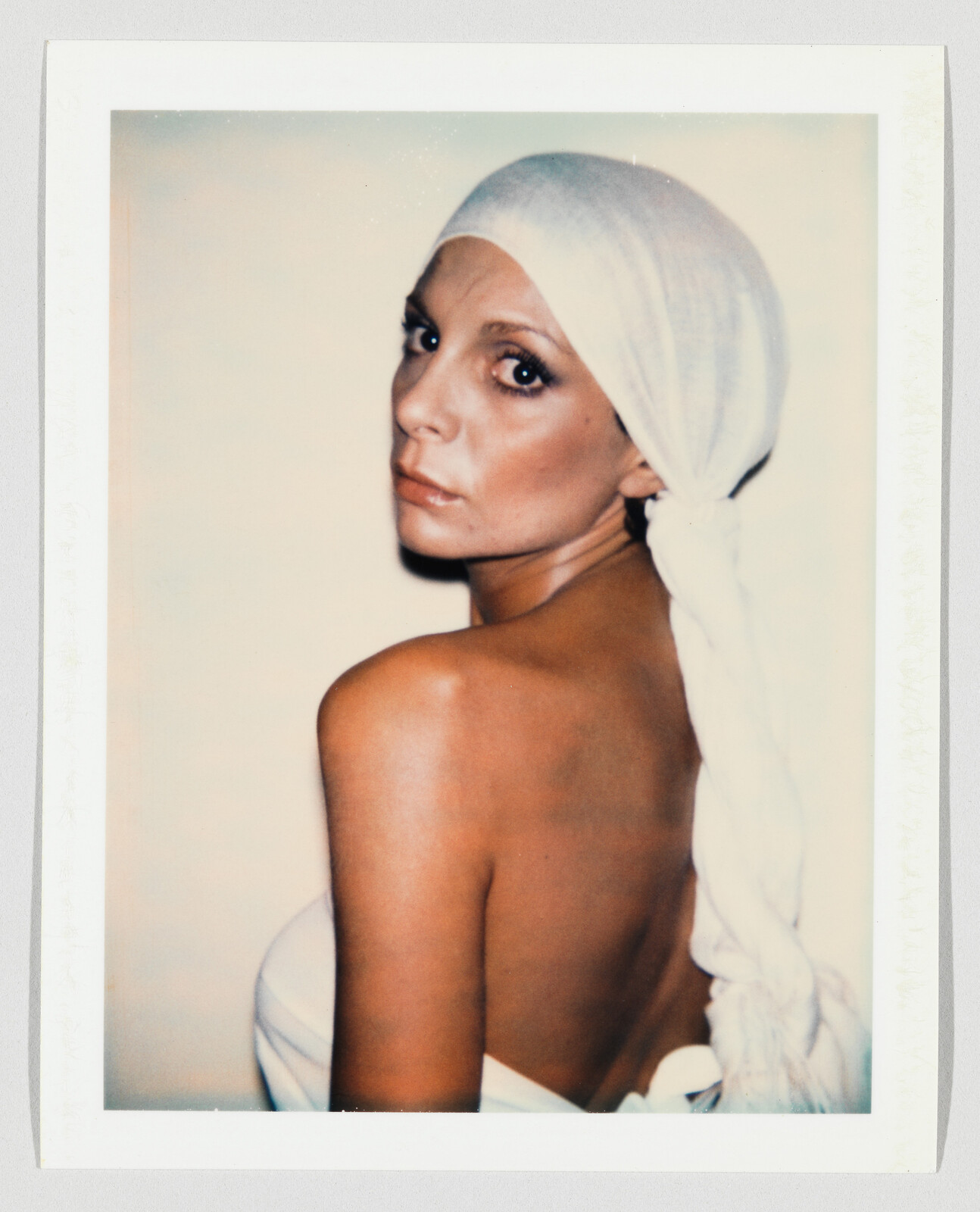 A woman with a white headscarf looks over her shoulder showing her bare back.